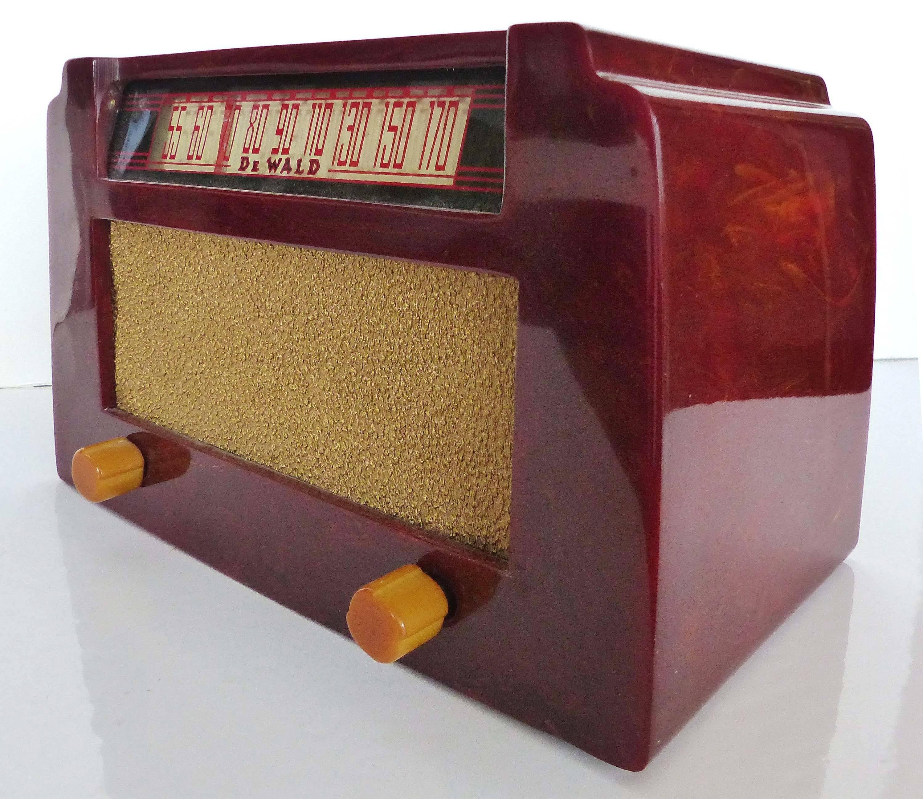 This clean American Art Deco Catalin A-502 radio known to collectors as the step top was made by DeWald Radio Manufacturing, Long Island, New York, circa 1946. The radio, in red with swirls and yellow knobs, is in excellent condition save for a