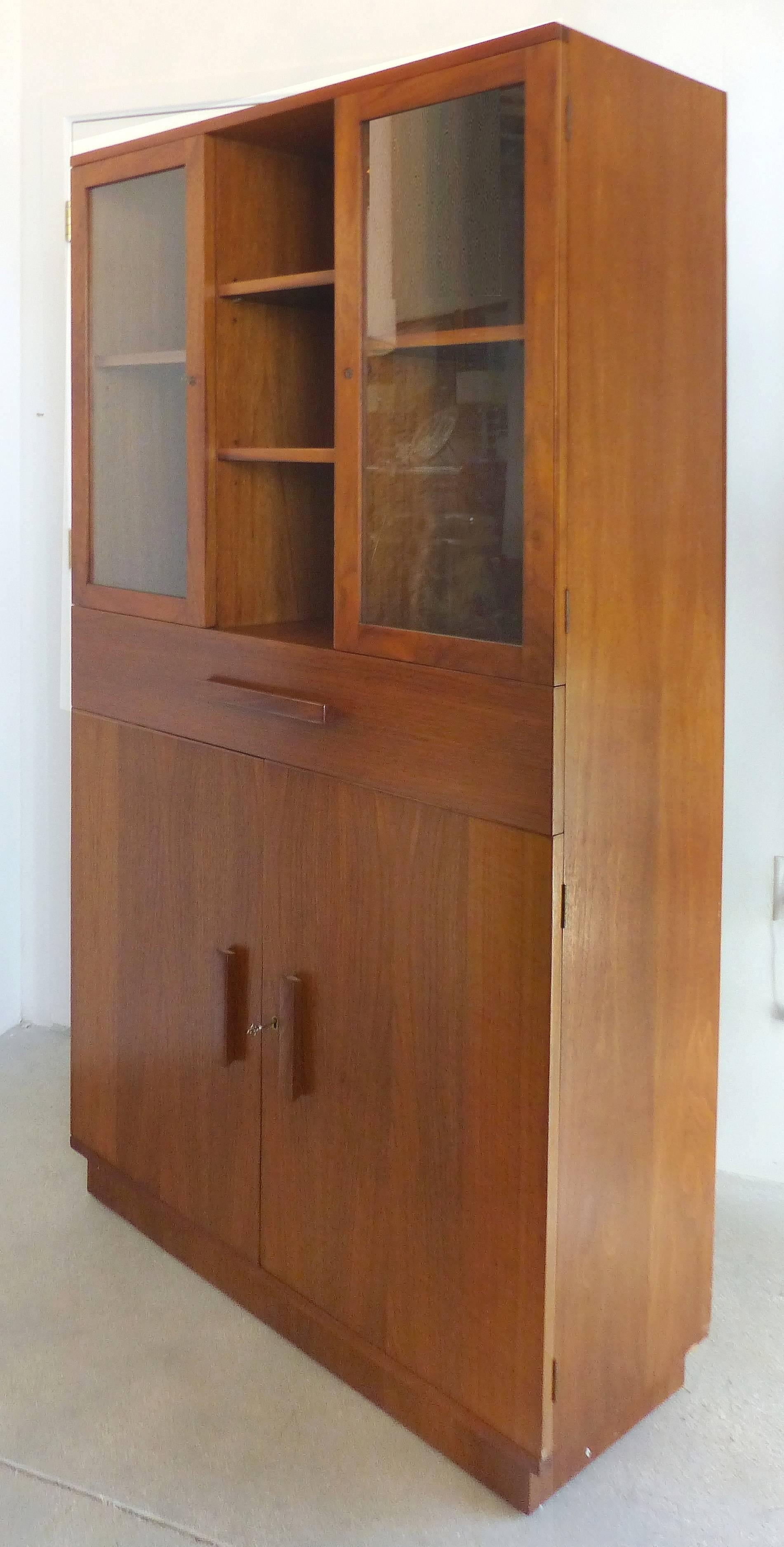 An American Art Deco bookcase vitrine cabinet manufactured and retailed by Modernage Furniture, New York, circa 1933. Created in American walnut veneers with solid walnut pulls. The cabinet has an indented foot, two doors on the bottom half open to