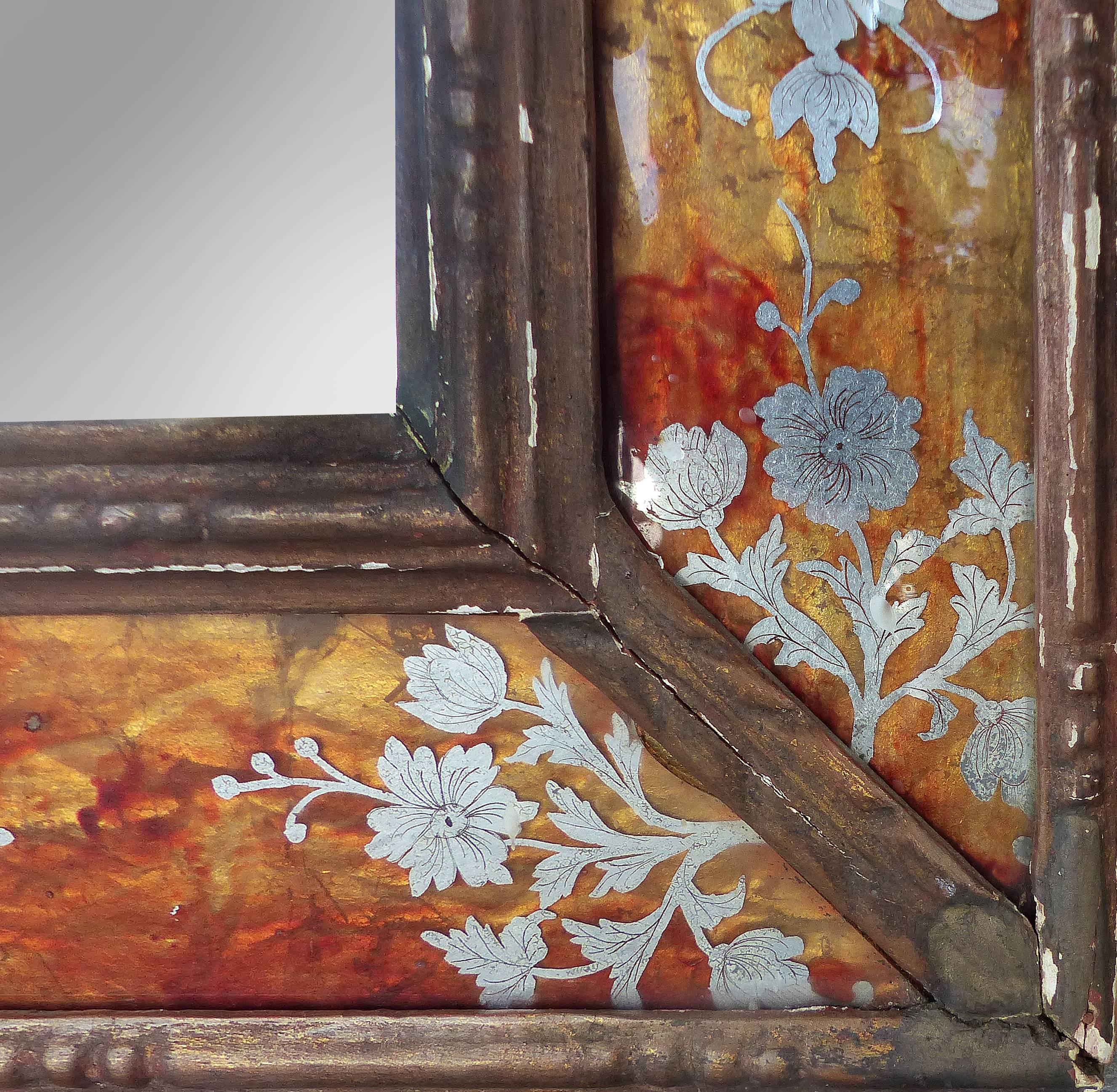 A striking 19th century antique mirror surrounded with églomisé panels. The glass panels are richly hued in bold contrast to the delicate silvered floral motif. Displayed in a carved wood frame which shows some finish flaking.
Verre Églomisé is a