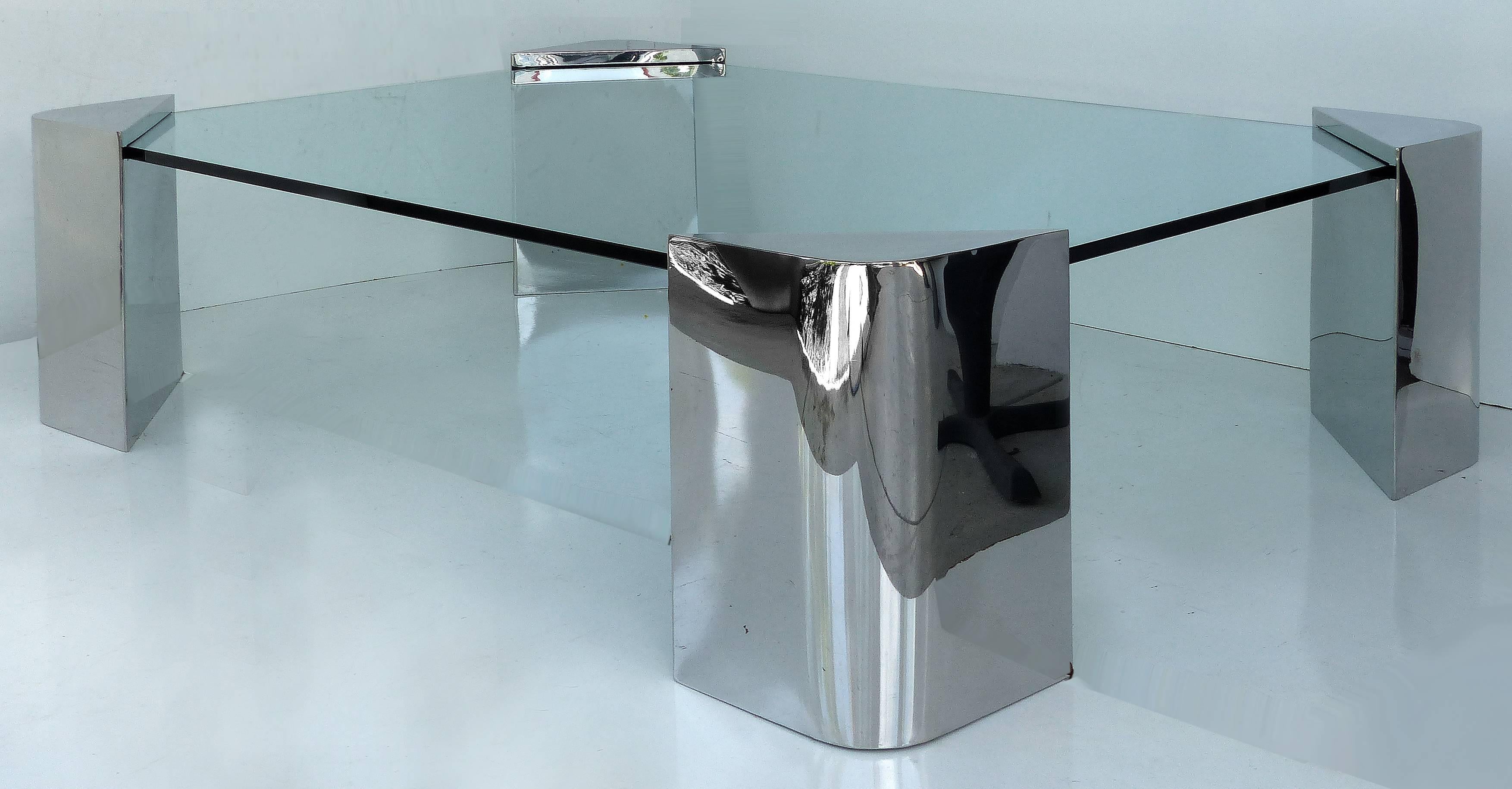 A large and substantial polished stainless steel and glass coffee table attributed to Karl Springer. Four stainless steel triangular corners supporting a 3/4" floating glass surface with a height of 18". In excellent vintage condition. The