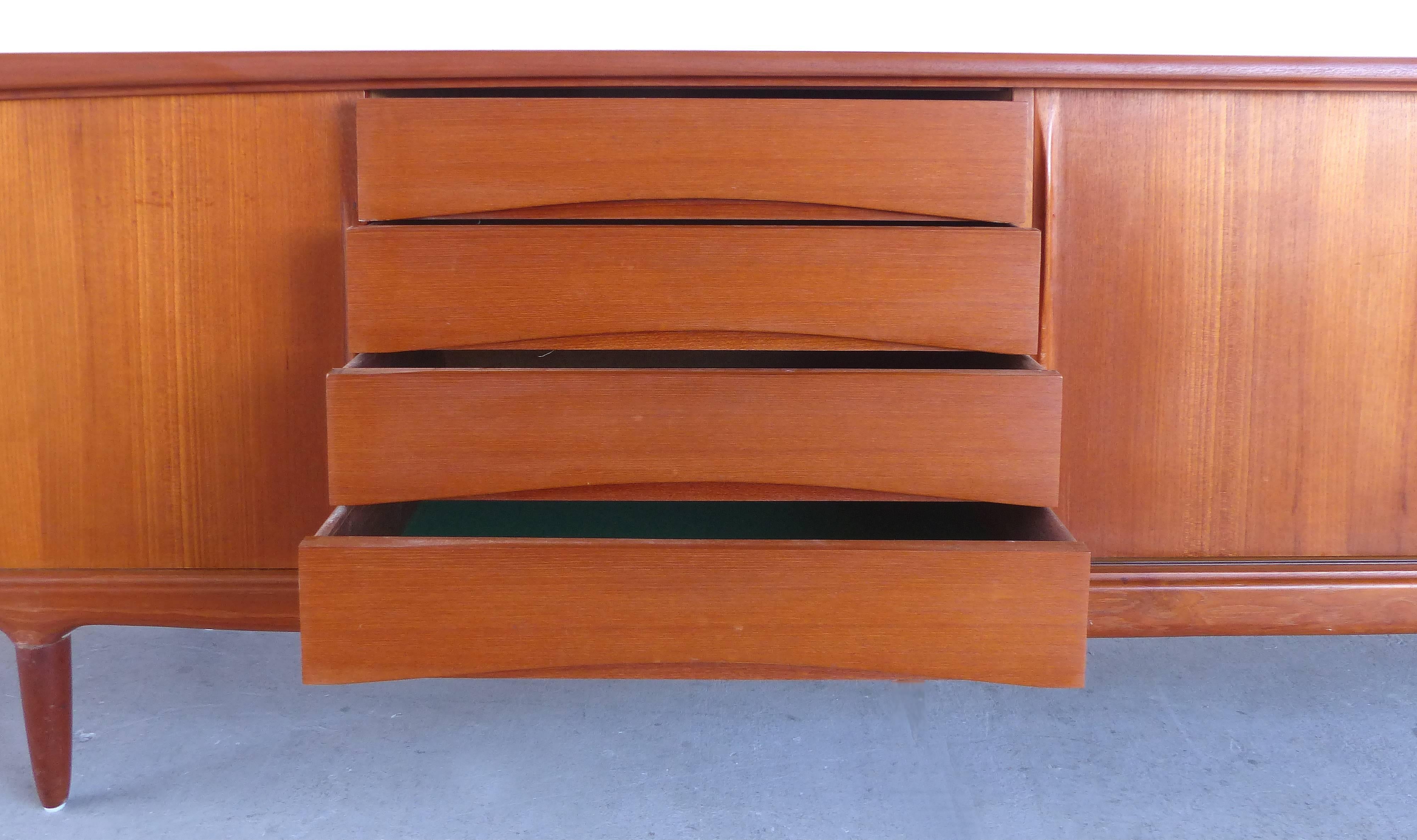 Offered for sale is a very laong iconic Danish modern credenza by Arne Vodder in teak. The credenza has sliding panels which are placed to reveal drawers and shelves. The drawers pull open from the recessed notches beneath the curved drawer fronts.