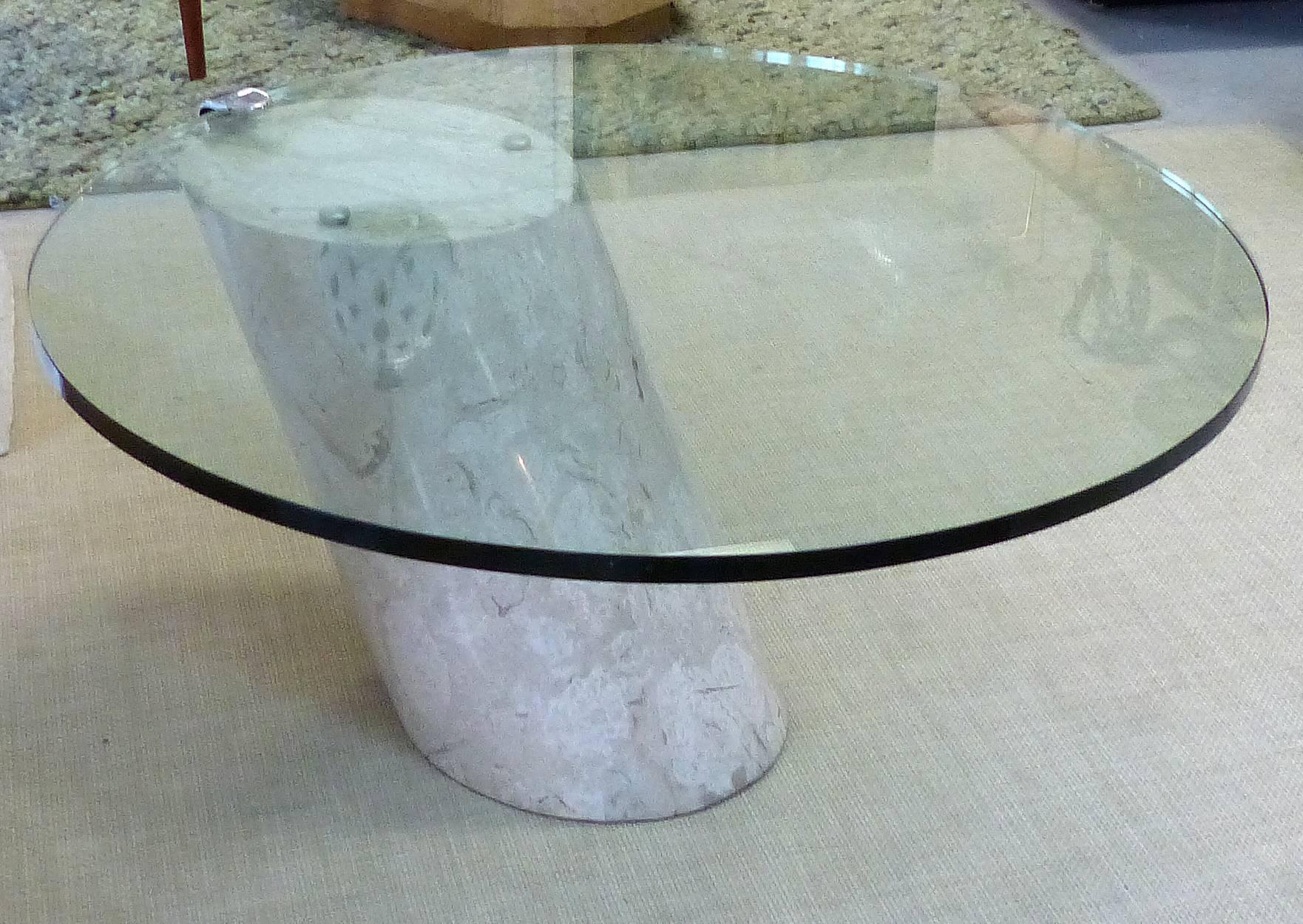 Offered for sale is a sculptural Travertine and glass cantilever coffee table by Brueton. The marble column counterbalances a thick round glass top which is held by a chrome bracket. Beneath that bracket there is a small chip that is not