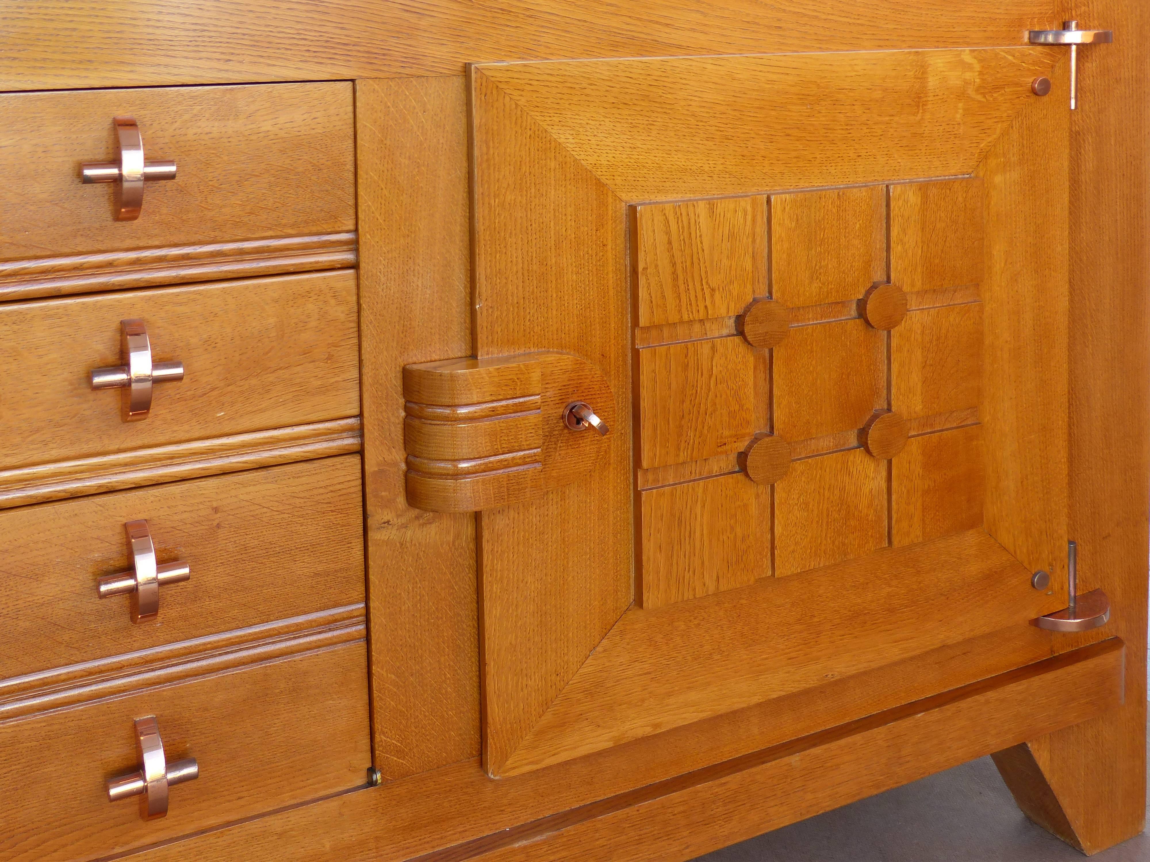 A French solid oak sideboard from the 1940s by Charles Dudouyt. A beautifully constructed cabinet with high-style copper hardware and elegant subtle carved details. Has two central drawers and a drop down compartment below. Flanked by two doors