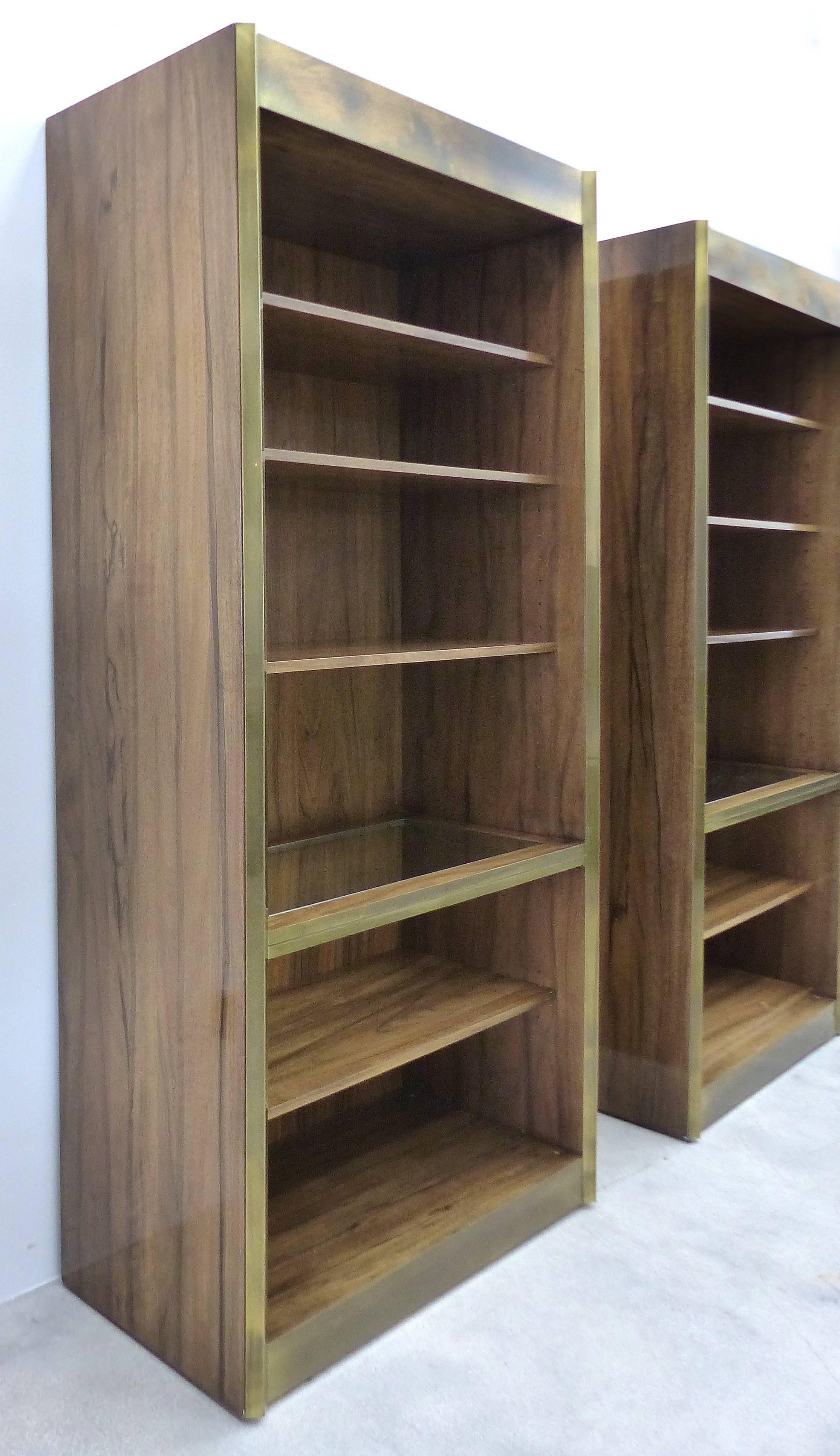

A pair of fine quality rosewood and brass trimmed bookcases by Mastercraft. Edged in angled brass with matching panels top and bottom, each bookcase has five shelves with one having an inset glass panel. Maker's mark on the back. The brass has a