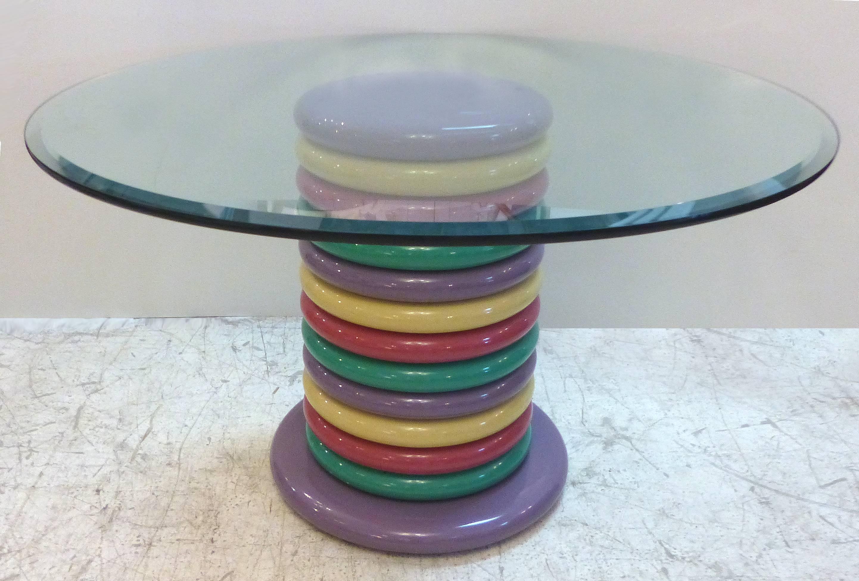A 1980s Memphis style multicolored table of round circular rings supporting a bevelled edge glass top. The wooden rings are highly lacquered and the glass top has a wide bevel.