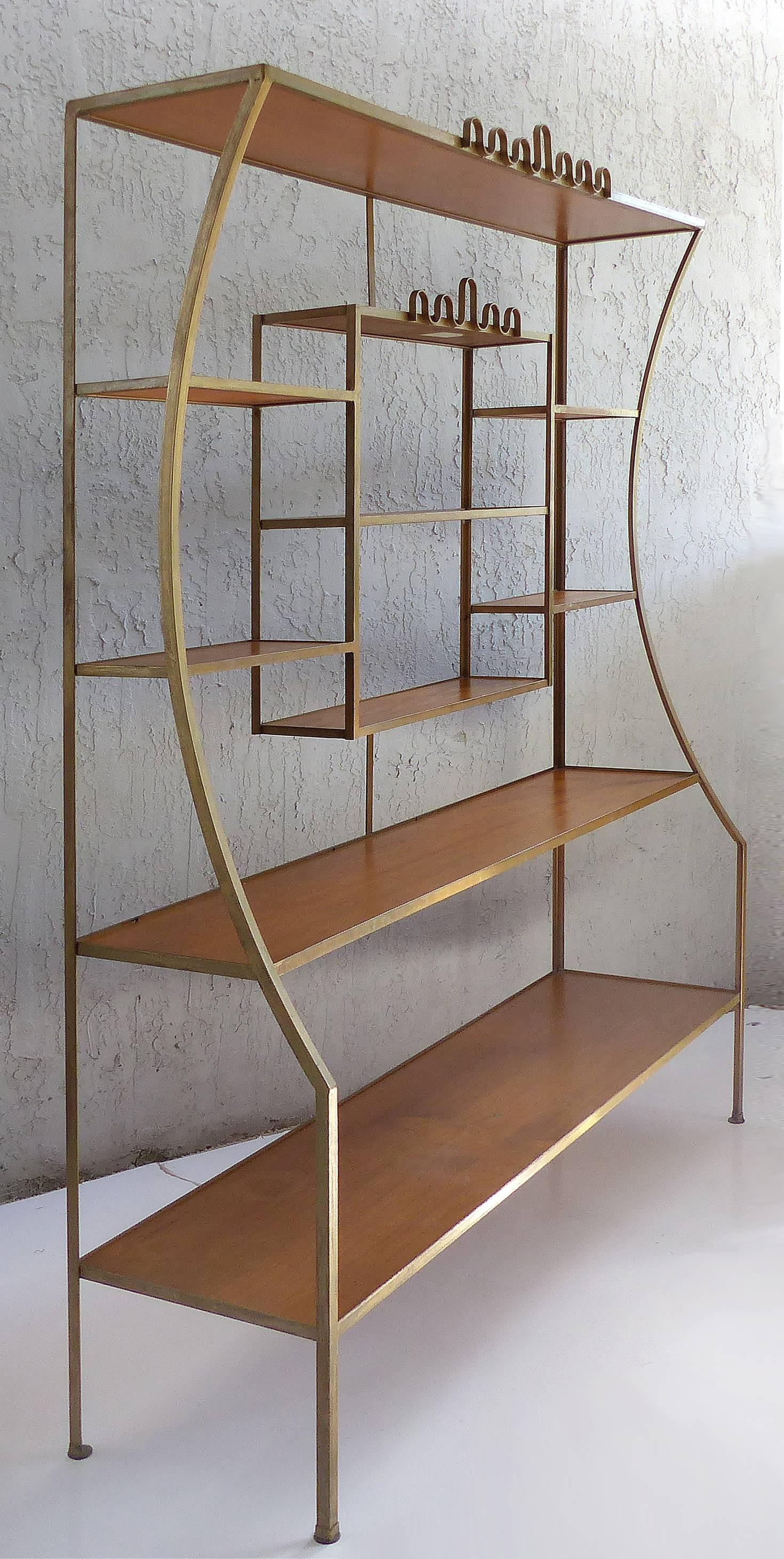 Offered for sale is an elegant Hollywood Regency gilt iron étagère attributed to Frederick Weinberg. The curved frame sides lead upward to a whimsical parapet detail. The frame supports two inset wood shelves, a shadow-box
with shelves and a
