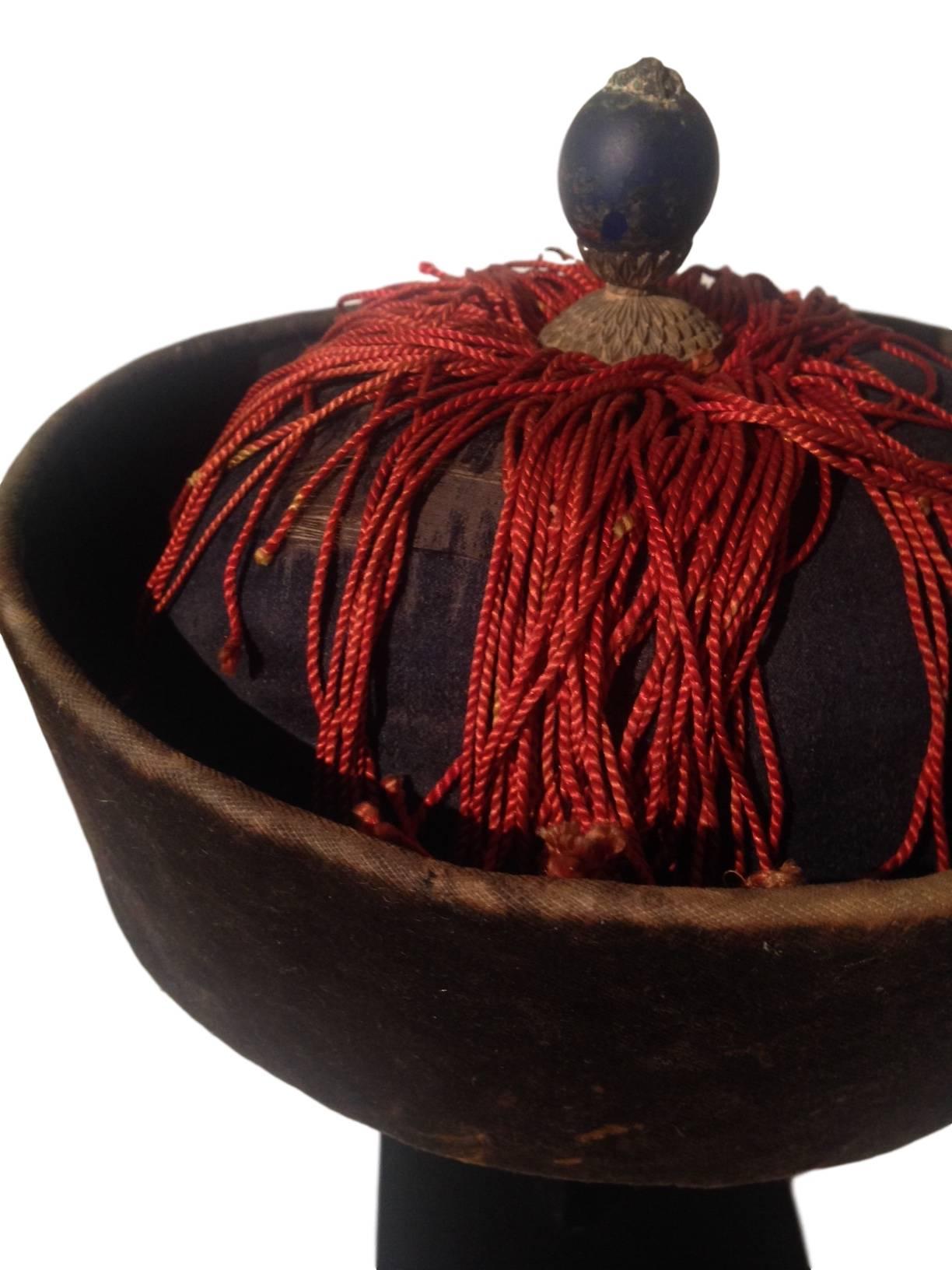 This 19th century Chinese court official's winter hat is made of soft black velvet and is covered with red silk fringe. The dark blue knob on the top indicates that this particular hat was a Qing official's hat and the knob is an imperial court cap