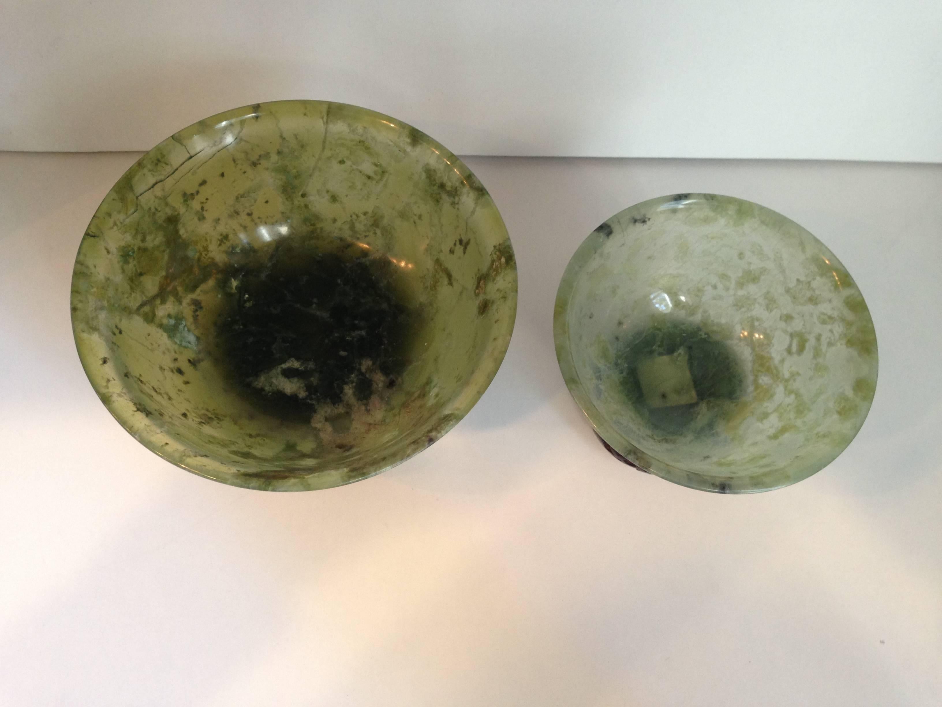 Pair of beautiful spinach jade bowls with deep sides and a slightly curved lip. Each bowls rest on a beautifully carved stands with rounded sides depicting floral patterns.