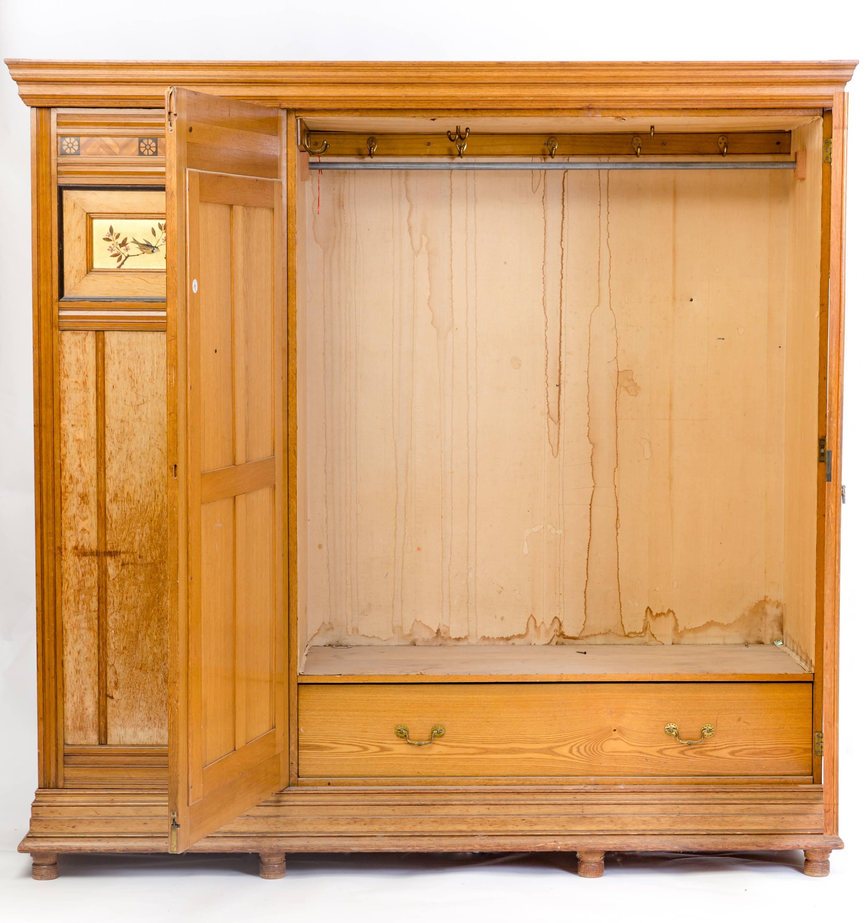 A large aesthetic ash wardrobe in the style of Charles Bevan dating to 1890. The front is beautifully inlaid with stylized flowers and painted bird motifs. The two doors flanking the central mirrored door are on turned feet. The mirror has a slight