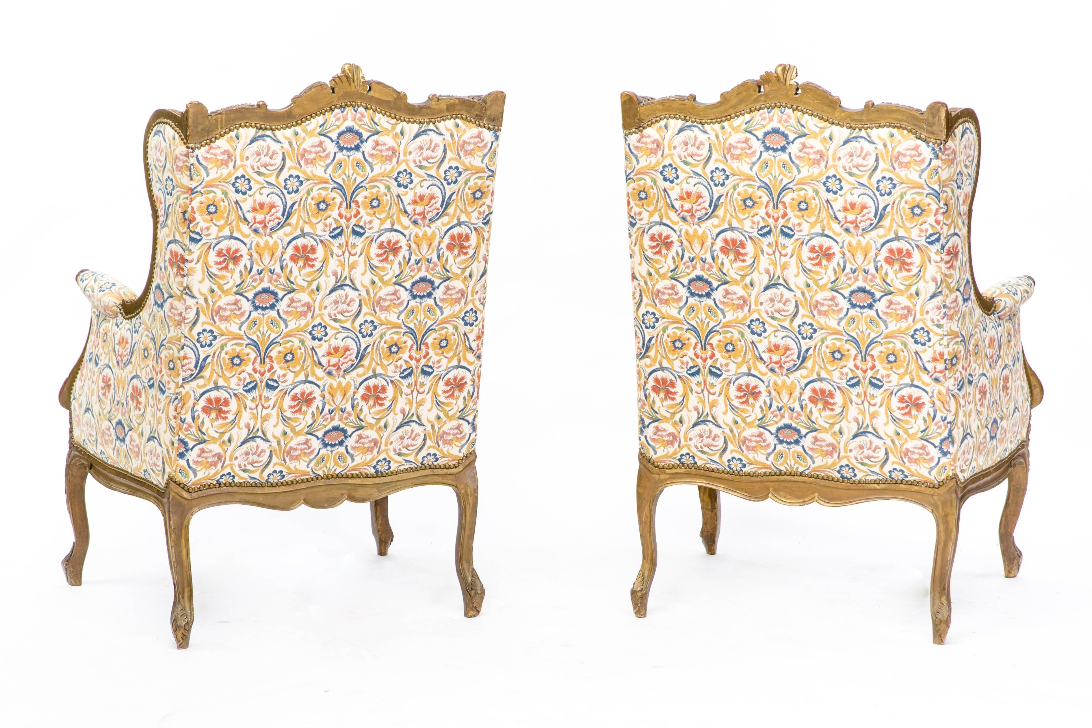 A stunning pair of 19th century Louis XV style French wingback armchairs upholstered in luxurious floral pattern, circa 1870. This piece is made of heavily carved walnut with a gold finish. Both of the items are in excellent condition.