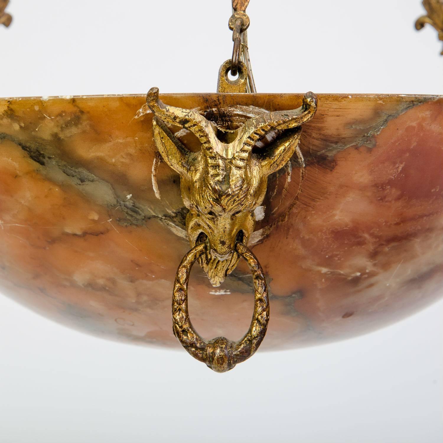 This 20th century amber alabaster light fixture hangs on ormolu mounts and decorated with heavily carved goat detailing and fleur-de-lis chains. 

Bowl dimensions: 4.25