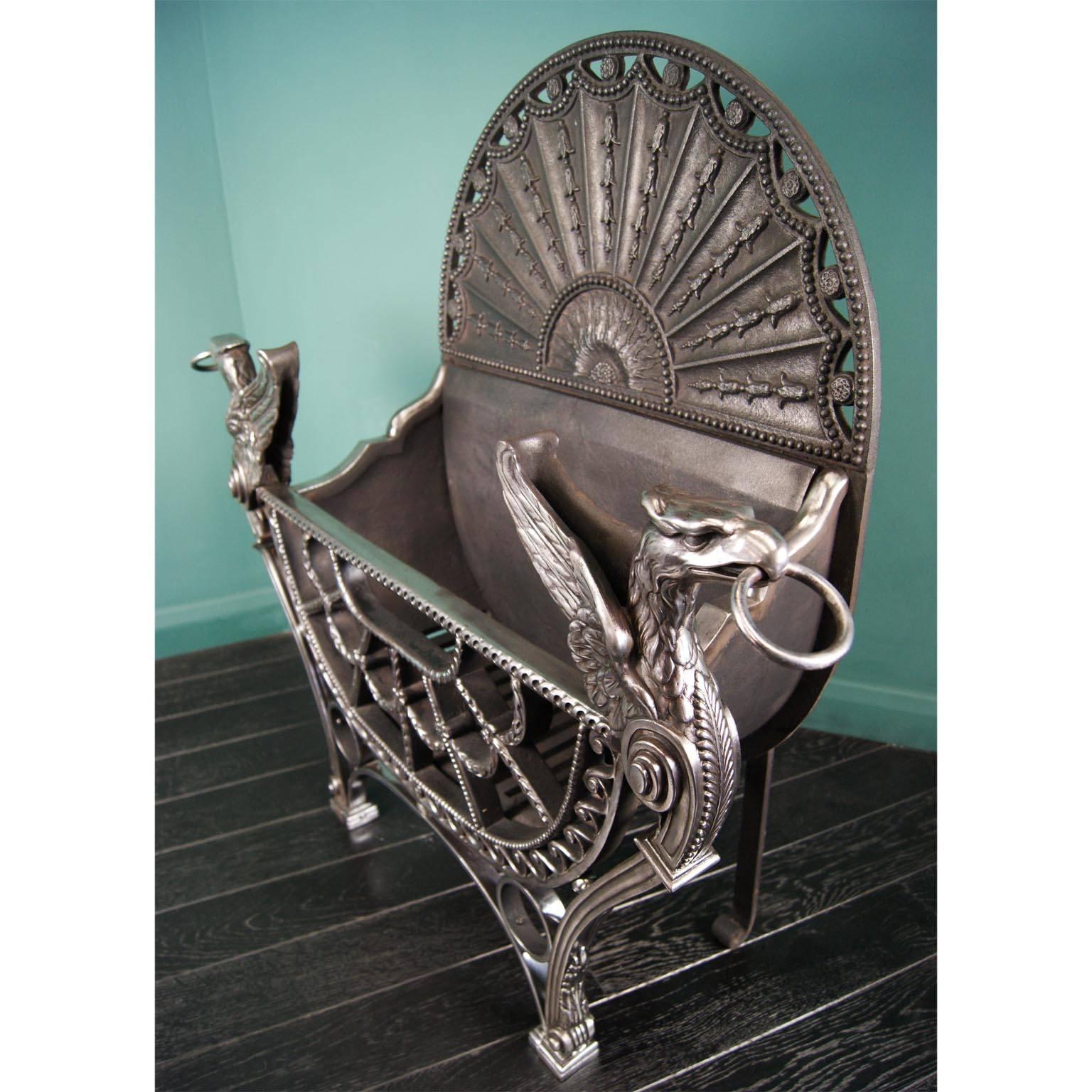 Large English polished wrought and cast iron fire grate in the Regency manner. The openwork fan-front basket is flanked by eagles, with a beaded Adam arched fire back, and bluebell drops in between radiating sunburst bars.