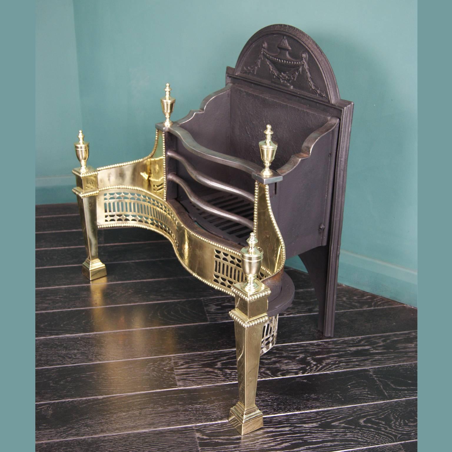 
A late 19th century brass and wrought fire grate in the 18th century manner of Robert Adam. The serpentine pierced fret is set between tapered legs with brass urn finials uppermost. Other details include polished wrought fire bars and fine
