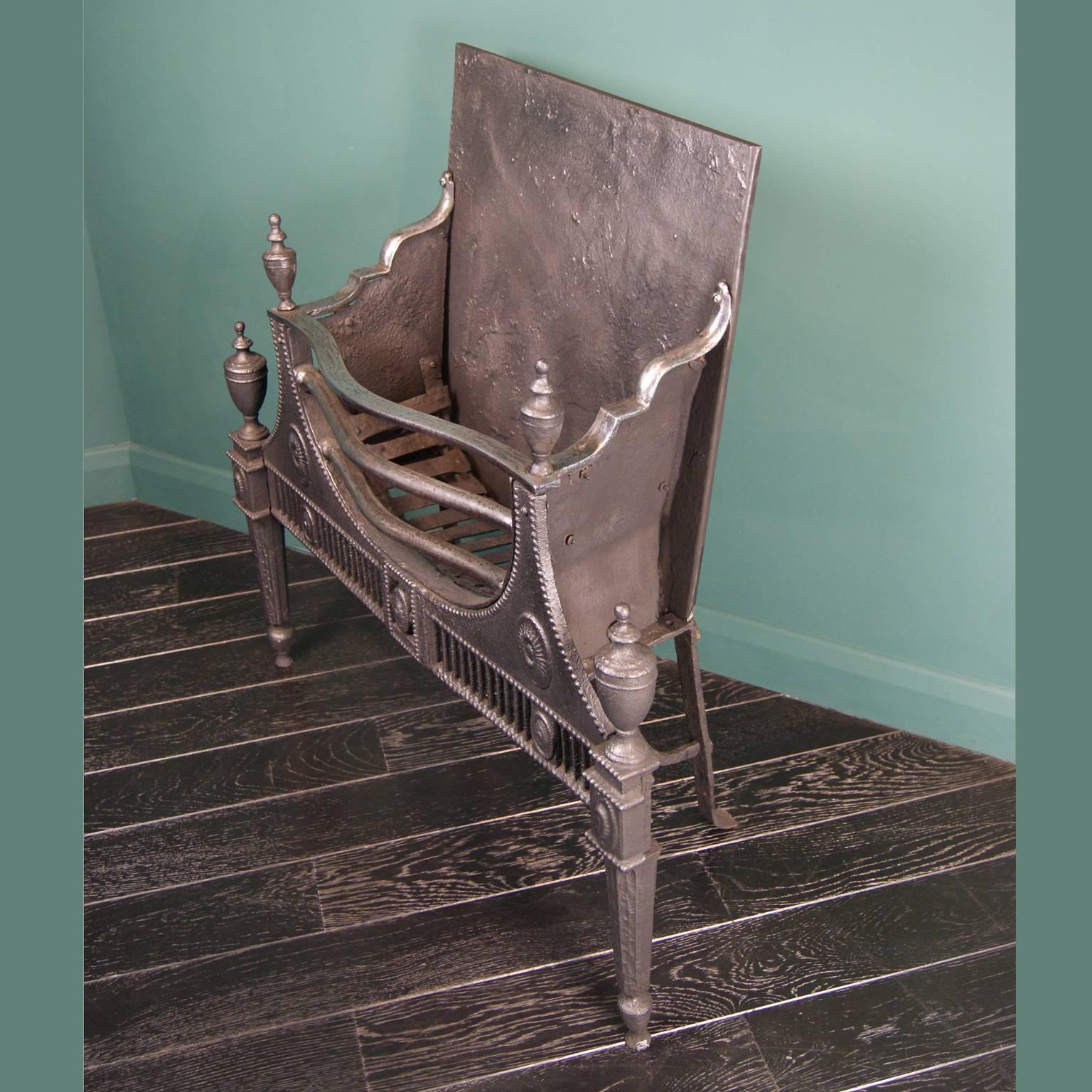 An 18th century cast and wrought iron neoclassical period fire grate. This grate has a decorative cast-iron front with bead, oval and flute detailing holding a semi-circular polished wrought iron basket. Tapered legs with urn finials uppermost and