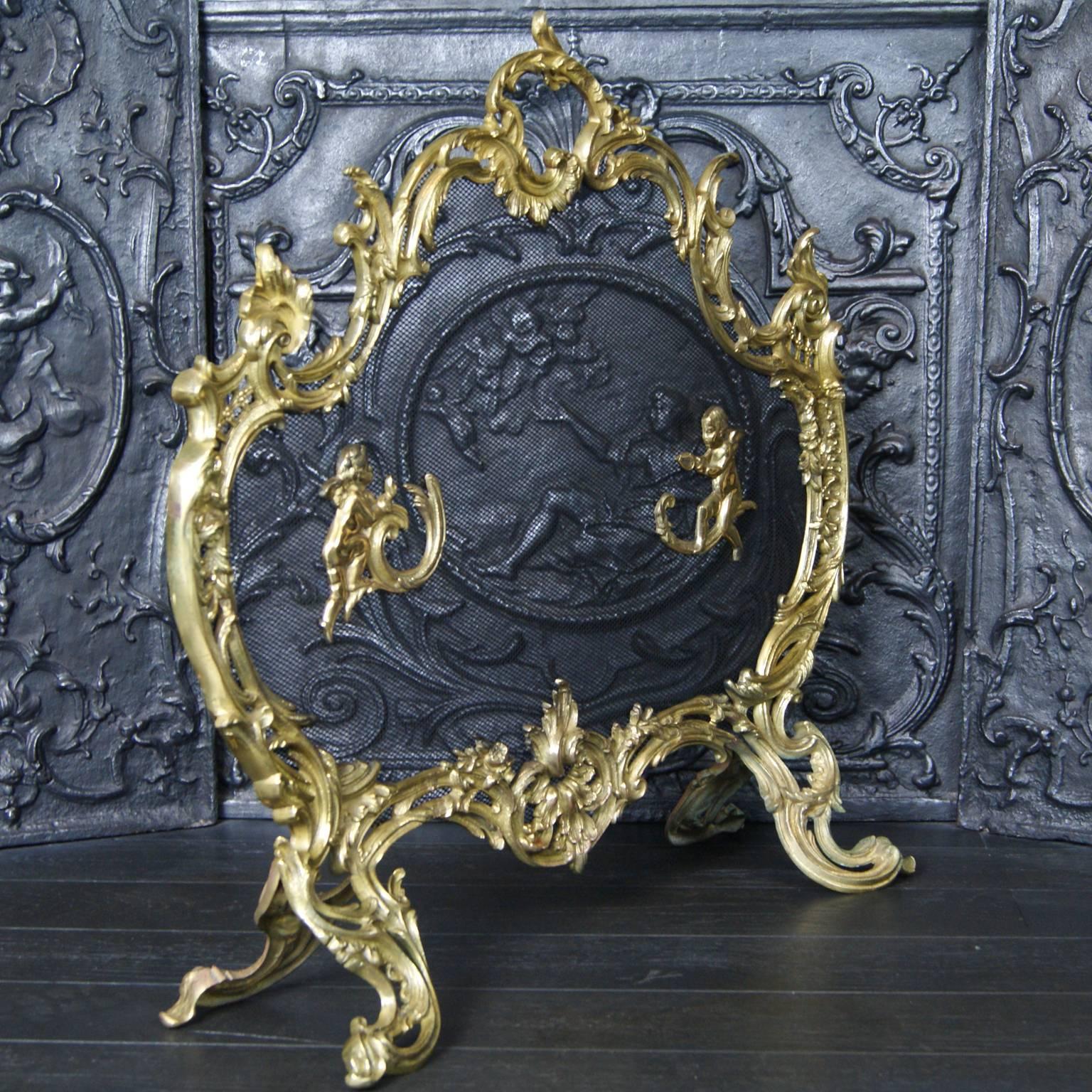A gilt brass Rococo fire screen. The frame with foliage and scrolling details. Two cherubs sit on the spark mesh.