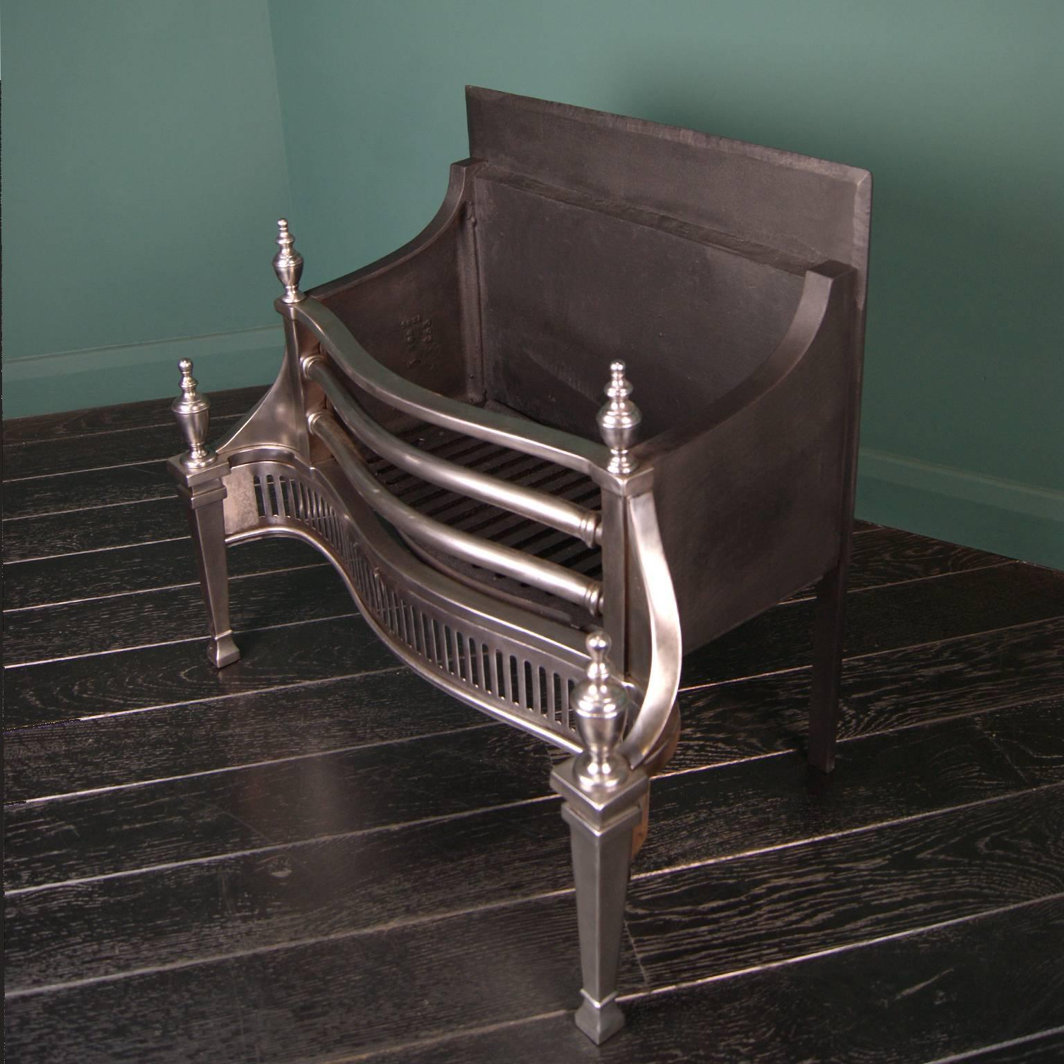 A polished steel dog grate from the Carron Company with pierced fluted fret and steel moulding, urn finials and tapered legs. A construction based on the designs of Robert Adam.