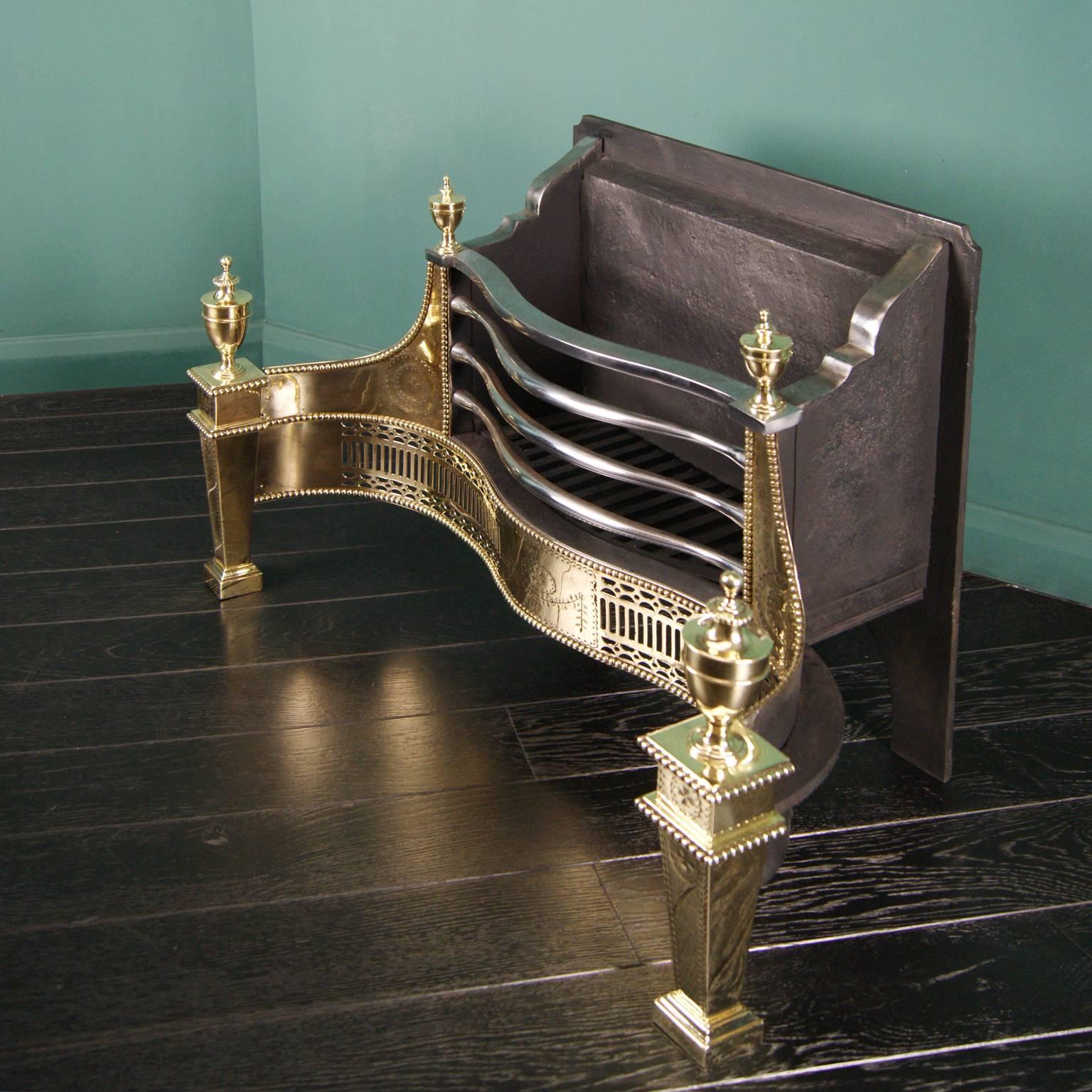 A large English Adam style polished brass fire grate (by Thomas Elsley). The fluted and pierced serpentine fret is set between square tapered legs with large brass urns. Fine engraving on wings, legs, and fret. This grate also features wrought-iron