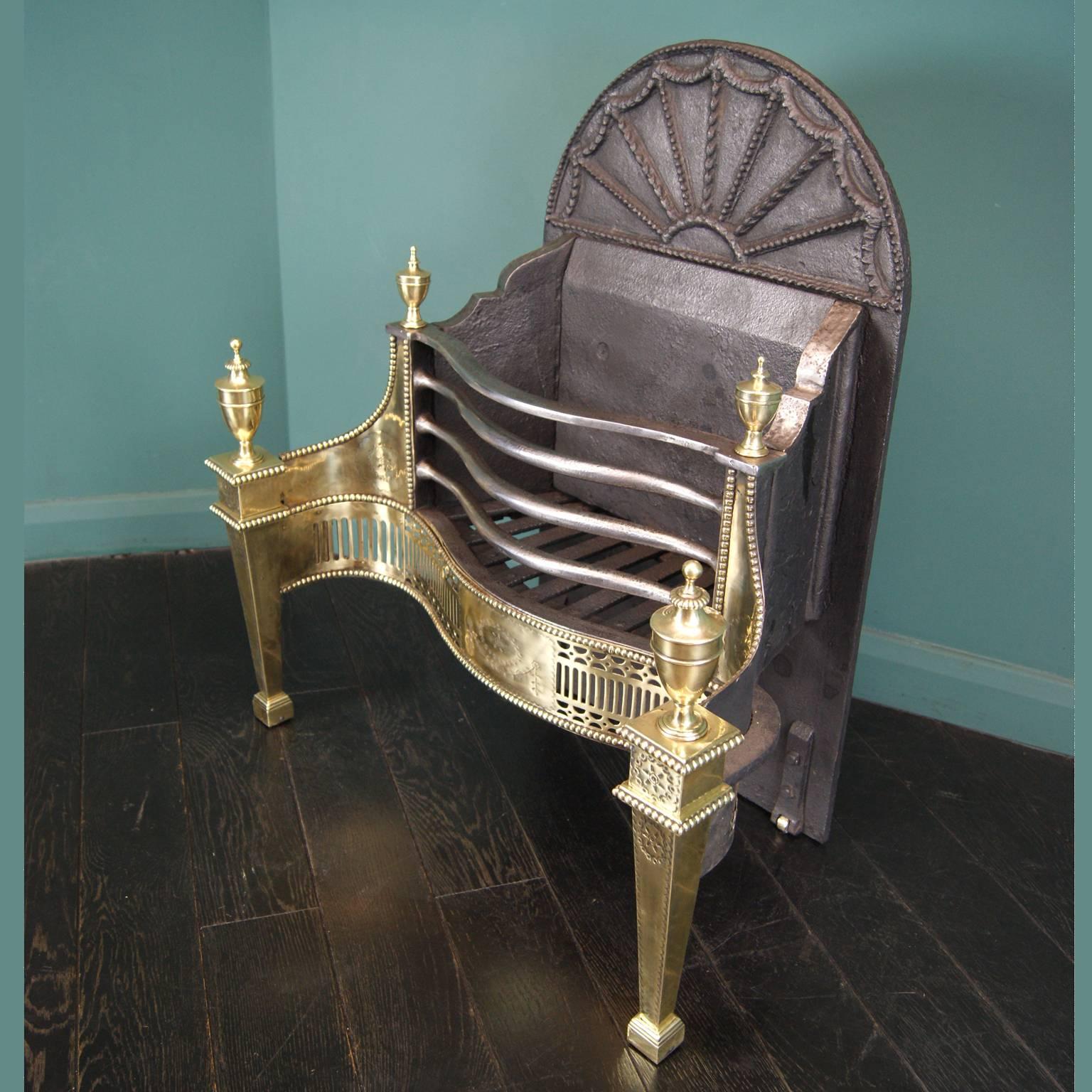 A polished brass fireplace dog grate by Thomas Elsley. The openwork serpentine fret is set between square tapered legs with large brass urns. Fine engraving on wings, legs, and centre. Wrought iron fire bars and an Adam arched fan fire back with