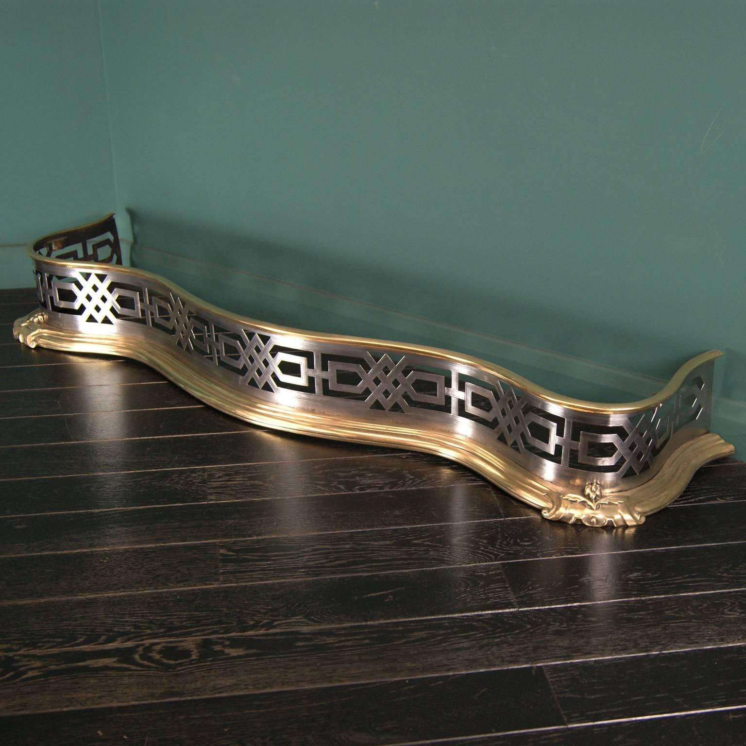 Polished brass and steel fireplace fender with geometric shaped openwork and linear engraving, set on a brass plinth and brass collar uppermost,

circa 1830.