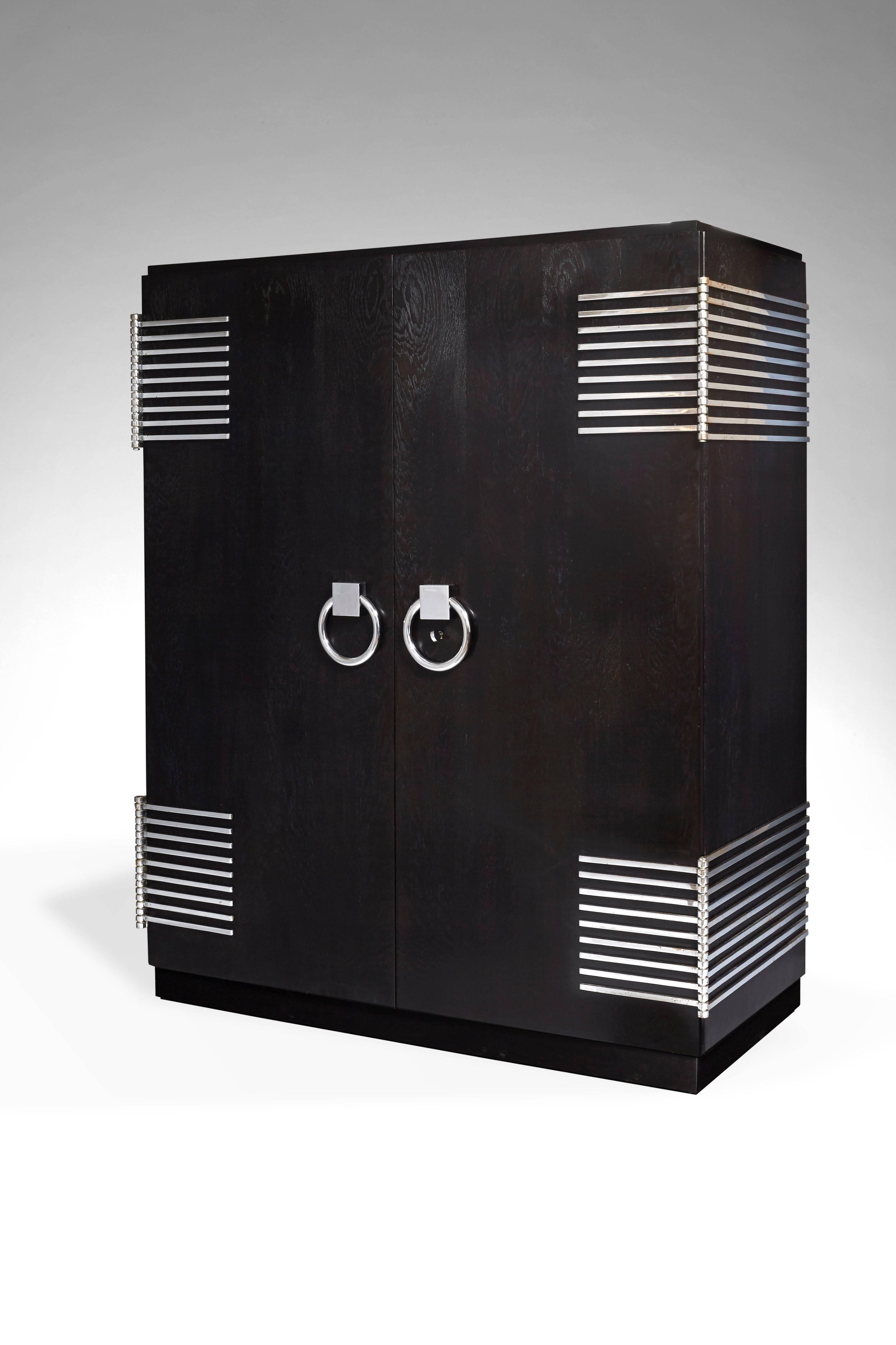 Designed for « La Maison L’Idéal ». Blackened and limed oak, hinges and handles in chromed metal, opening with two doors discovering an oak interior with a wardrobe and four drawers. The metal rod engraved « L’IDEAL ».

- Mobilier et Décoration,