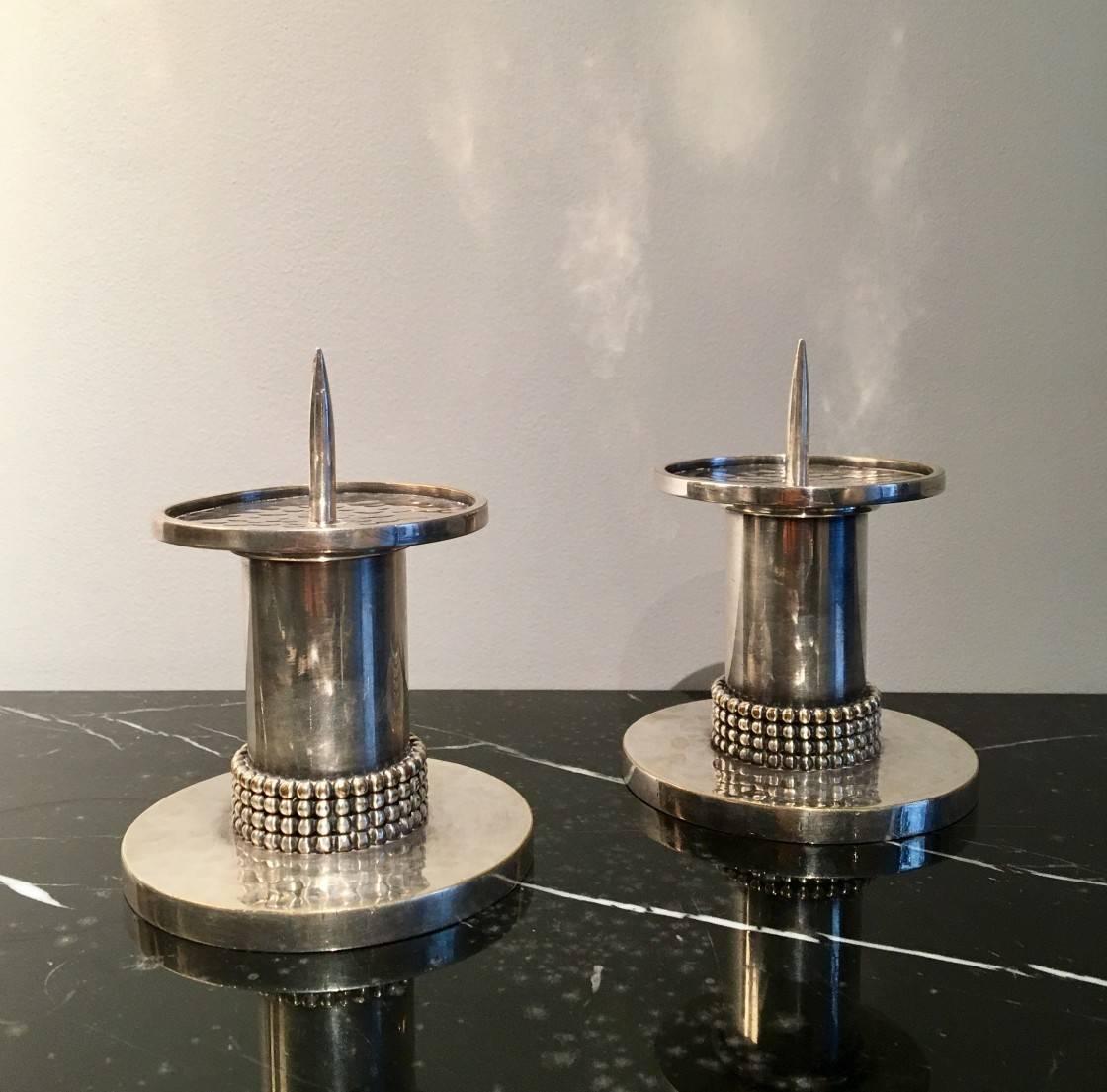 A round-shaped pair of candle spike in silvered partly hammered metal. The base decorated with four superposed rows of small balls. Signed under the base.