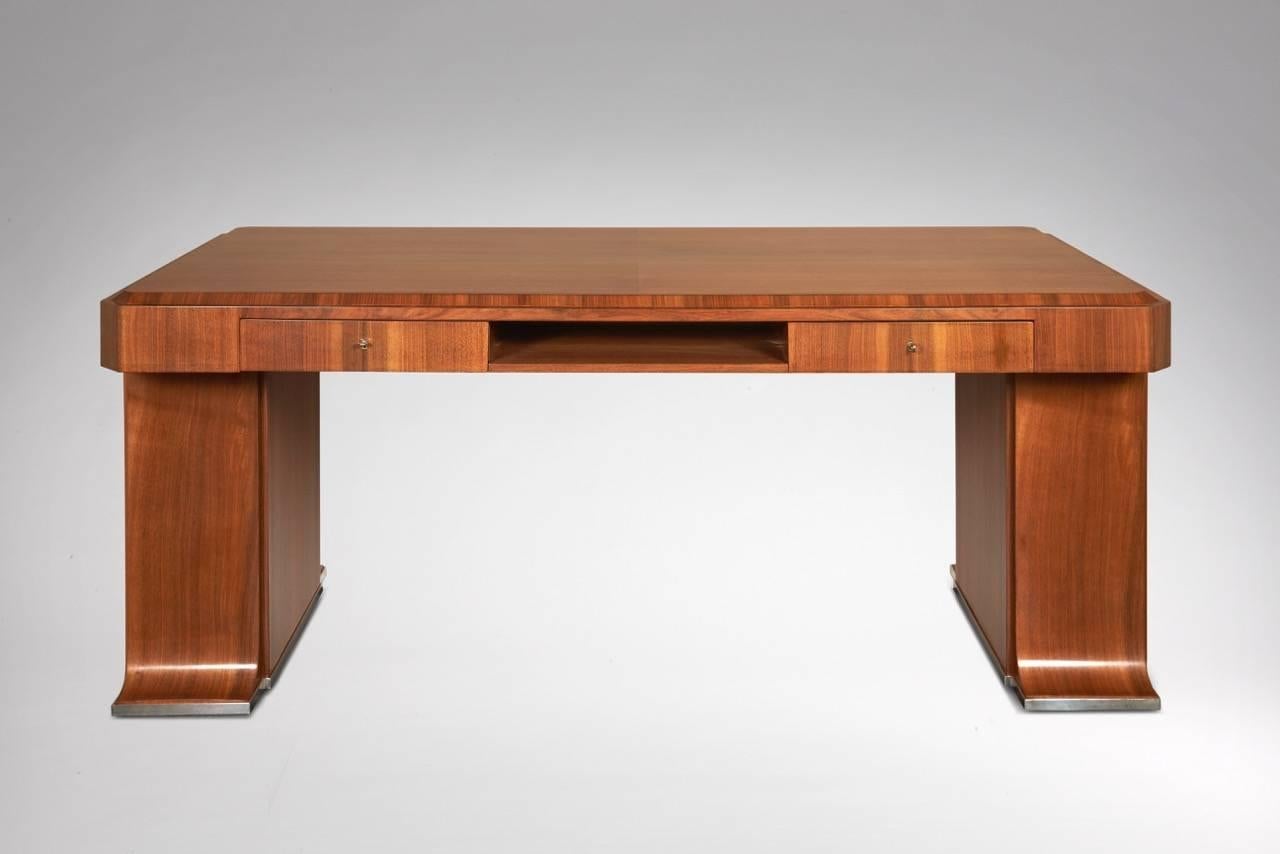 Desk in wood veneer with a rectangular top, opening by two lateral drawers and an open box in the front. Lateral legs opening with two doors on an interior with shelves. Quadrangular silver-plated metal plates at the belt, the legs highlighted by a