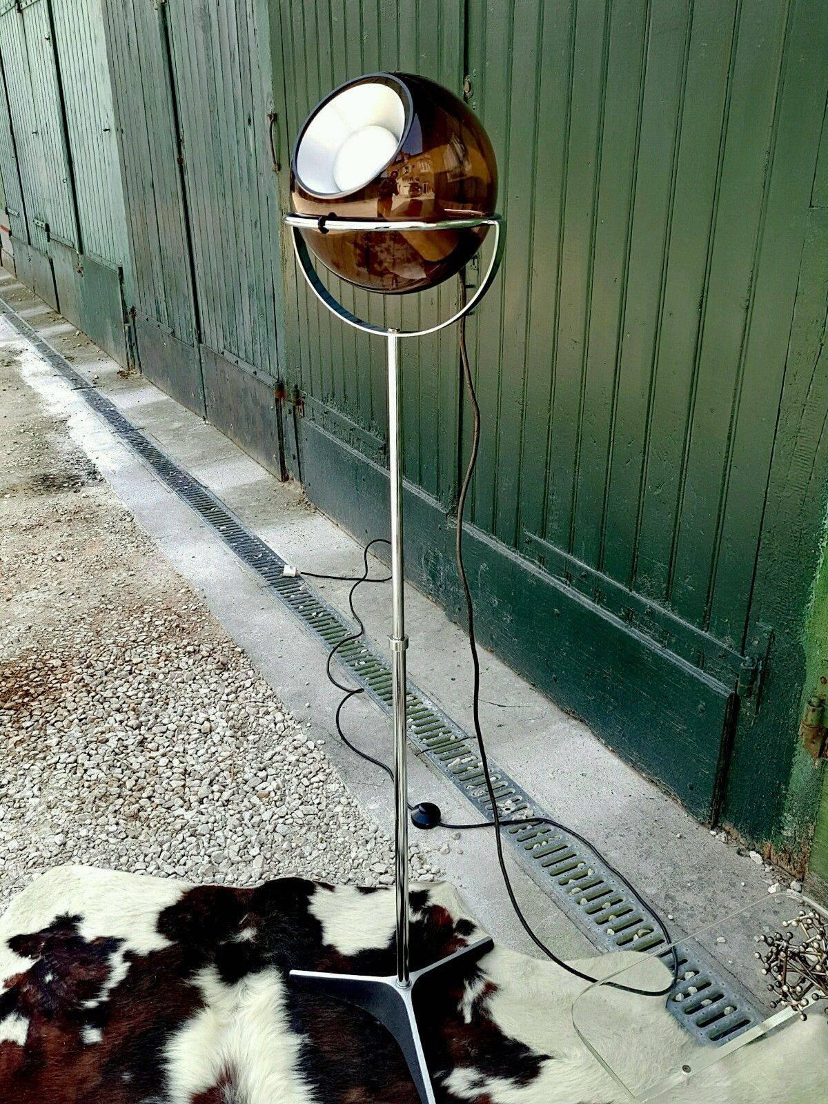 This chromium-plate steel floor lamp has a pivoting smoked glass globe on a height adjustable tripod foot. It is a design of Frank Ligtelijn for Raak Amsterdam in 1961. The glass sphere can be lifted from the ring and turned in any direction. The
