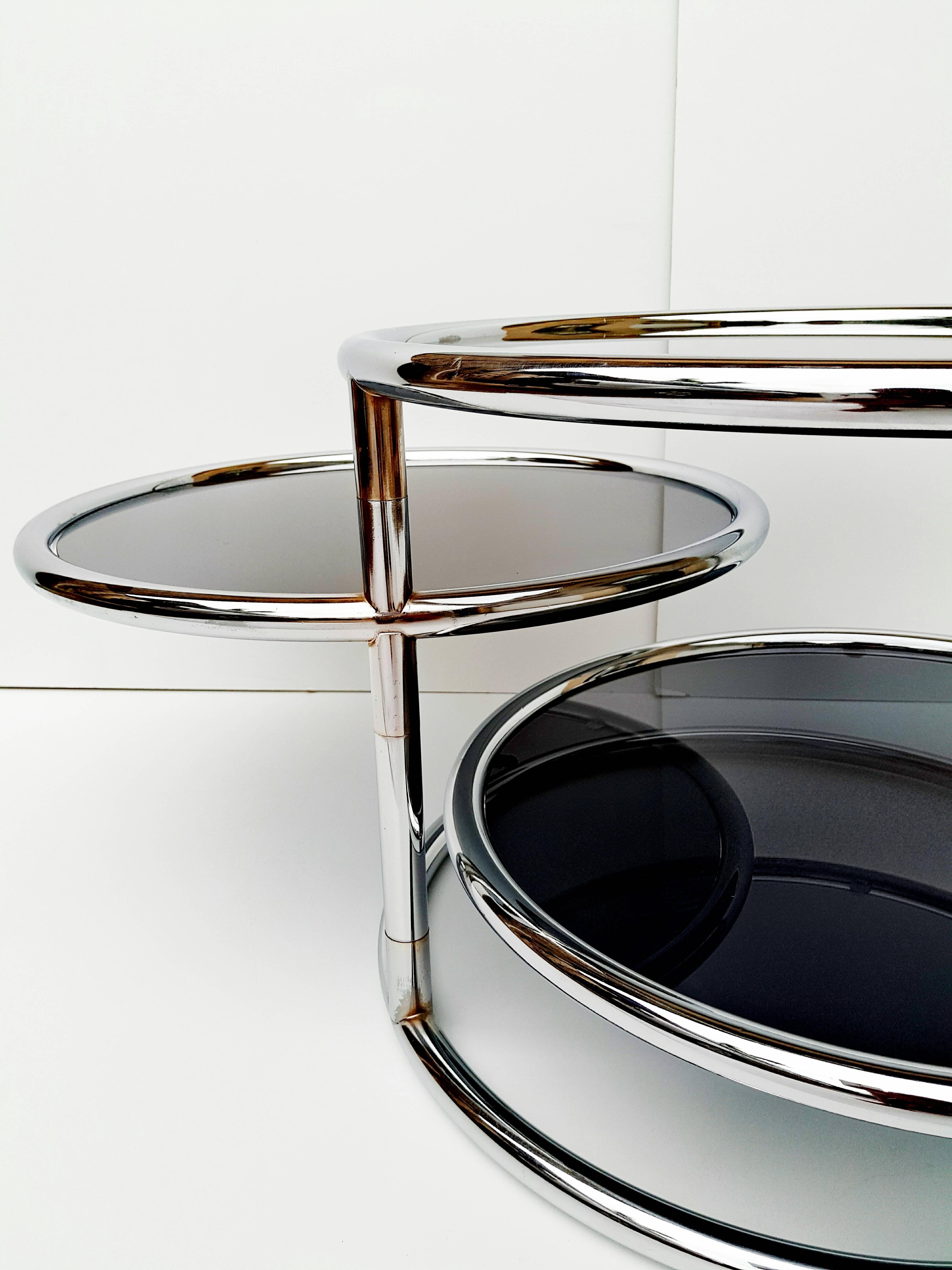 Attractive Mid-Century chrome and glass three-tier mechanical cocktail table attributed to Milo Baughman.
This coffee table features three tubular chrome and dark glass surfaces. Two top both swivel independently allowing the table to expand in