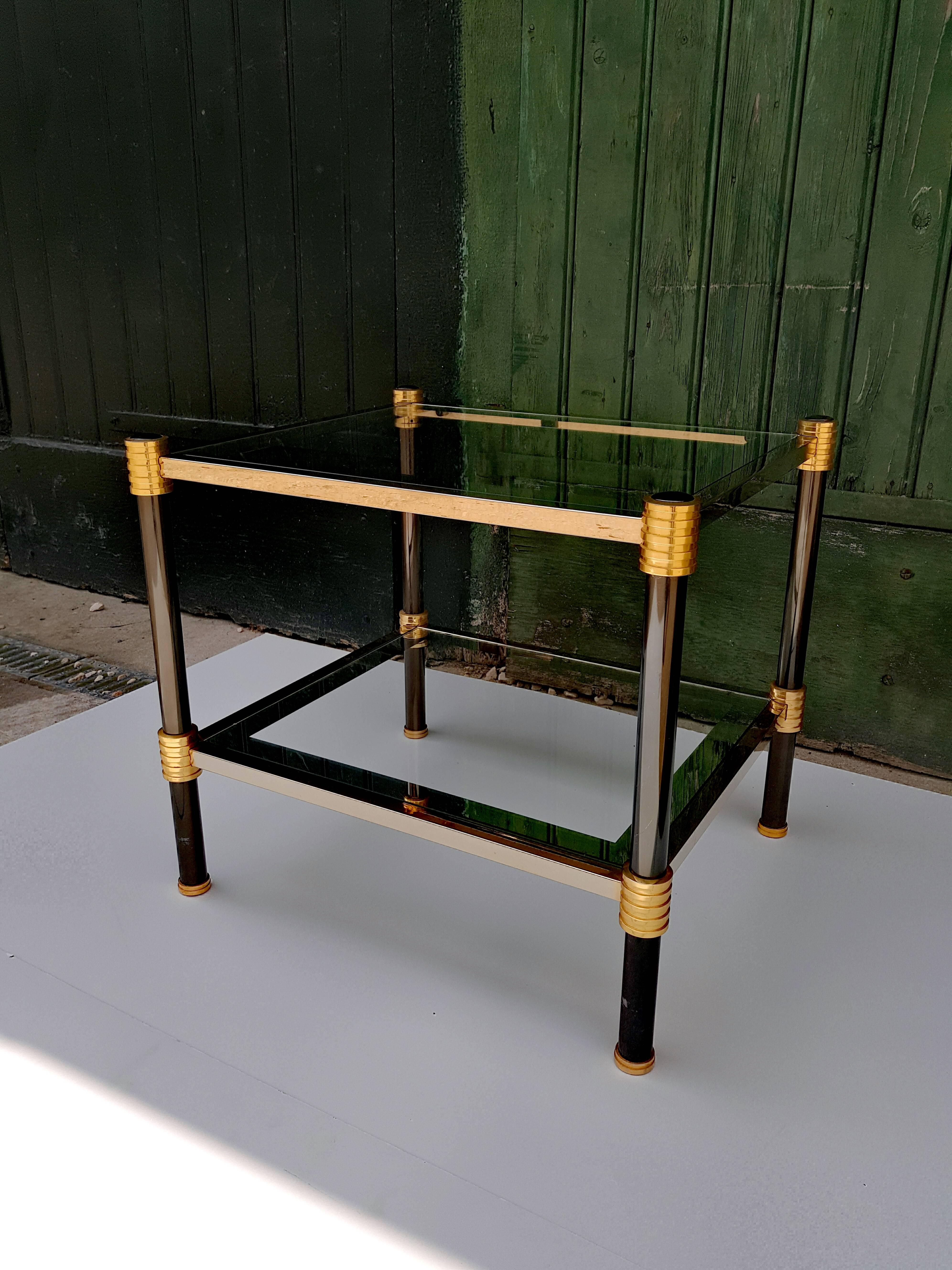 Mid-century French vintage end table by Maison Raphael, with black metal legs, brass feet, and finely cast brass strilled corners holding two glass shelves with mirrored edges. A wonderful table with all the beautiful whims of its era.