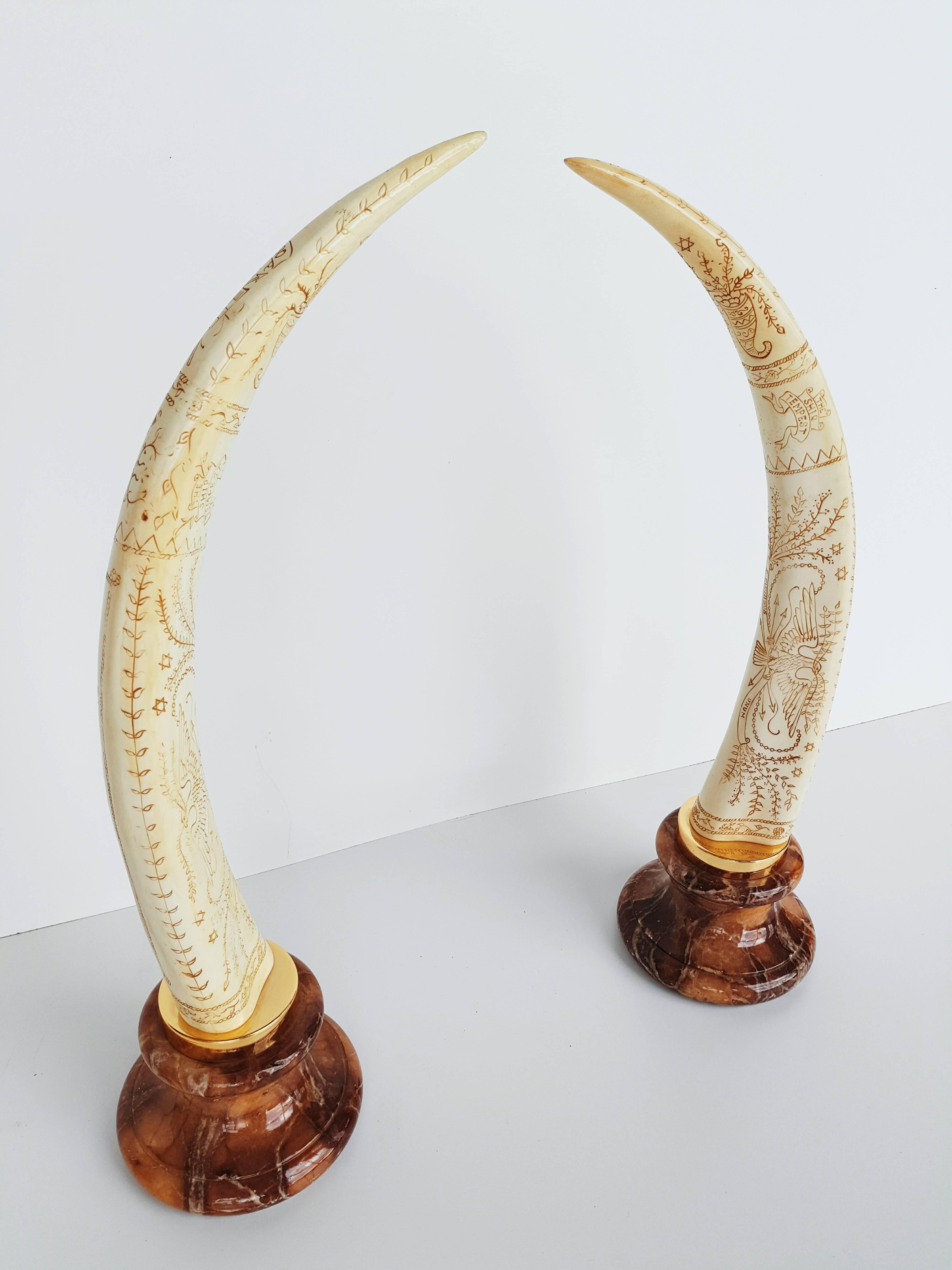 A pair of resin elephant tusk form arches with brass fittings and a marble plinth base, circa 1970s. Please note; these pieces are not real ivory. They are decorative resin replicas.
