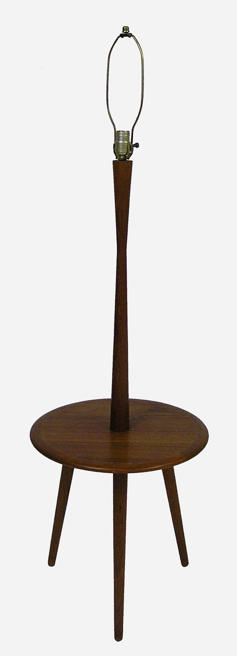 A stylish tripod-leg teak floor lamp with attached elliptical table from the 1960s. Gorgeous Danish modern inspired lines featuring tapered conical legs and fitted with a three-way fixture. Shade shown in last picture is not the original and is not