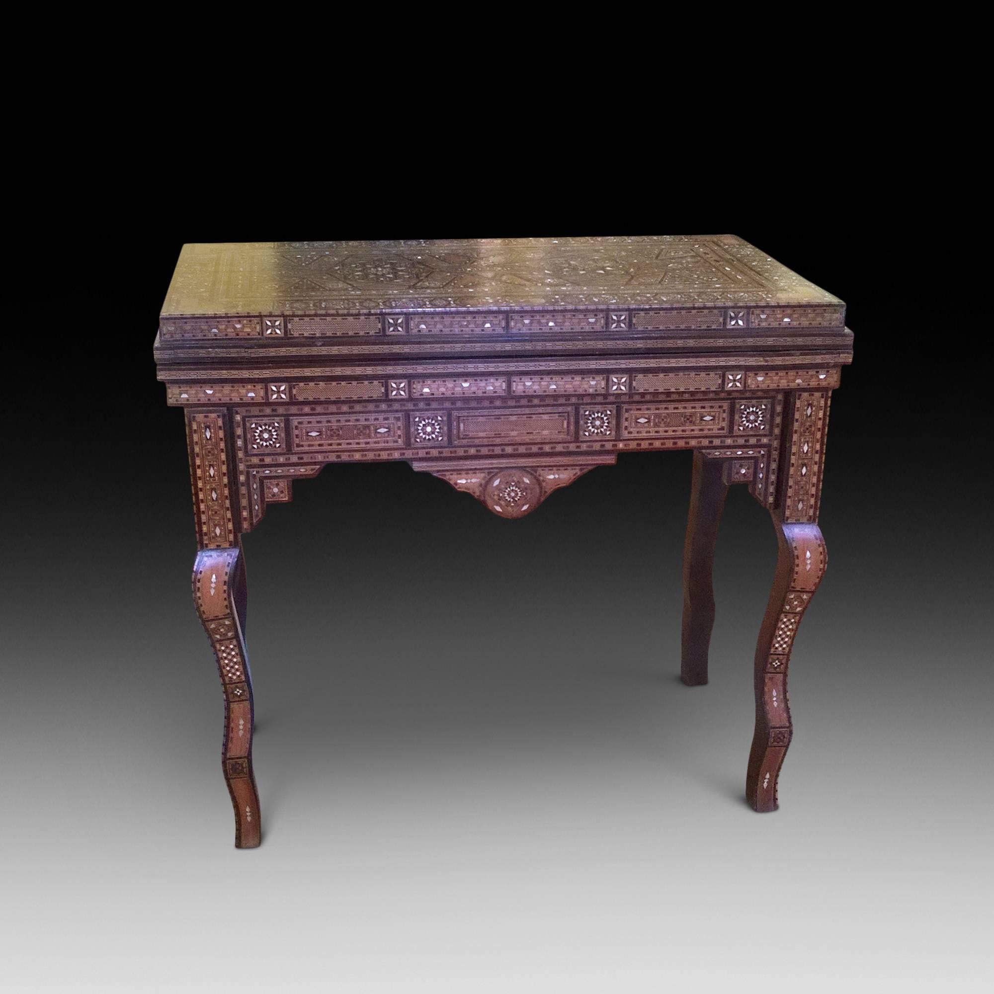 A Persian marquetry rectangular games table for cards, chess, chequers and backgammon - folding top enclosing an inset playing surface and an arrangement of compartments with sliding covers, profusely inlaid overall in the Moorish taste with