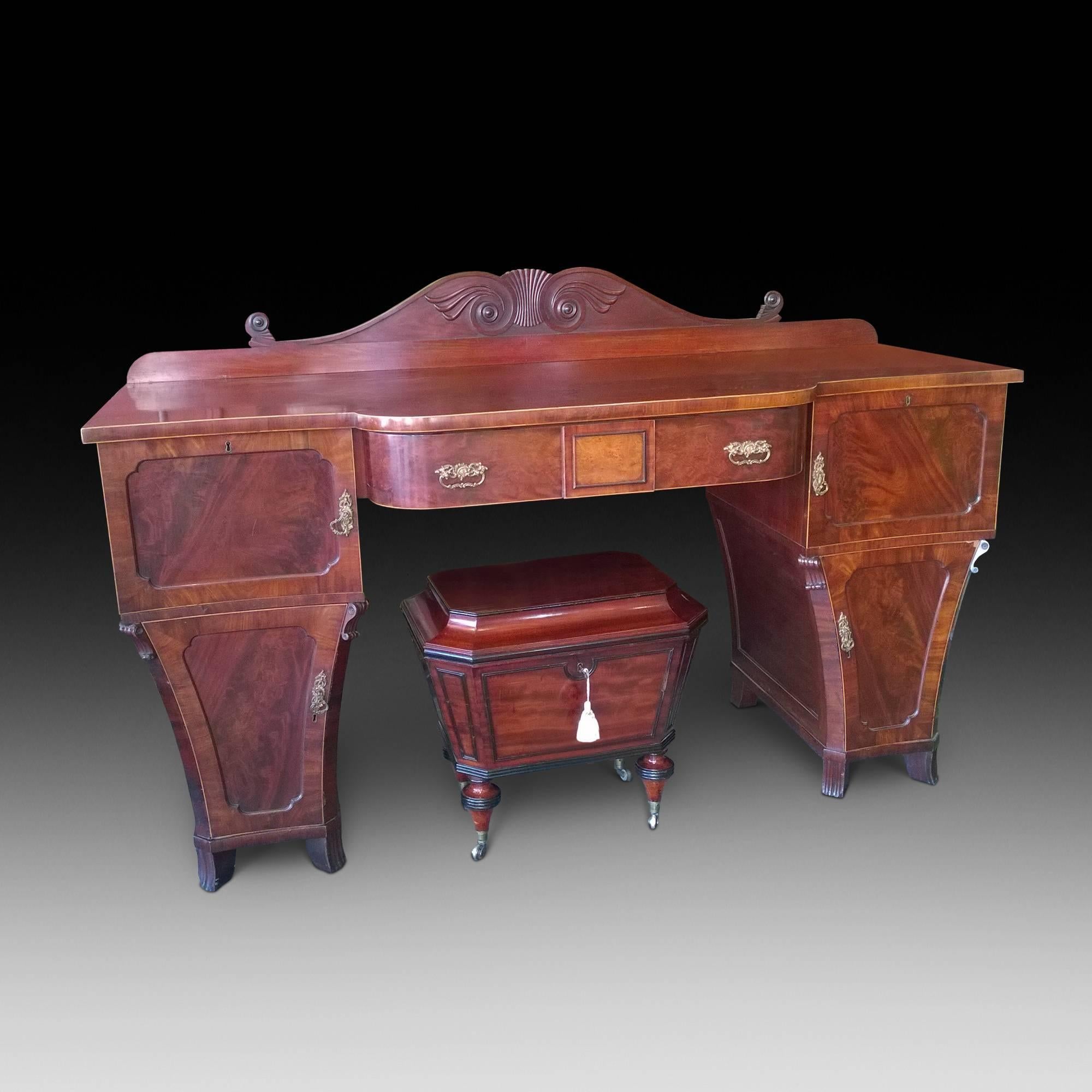 Regency mahogany pedestal breakfront sideboard with shaped back, satinwood stinging, decorative brass plate handles, and concave bowed doors to the cabinets and cellaret drawer. Measures: 73