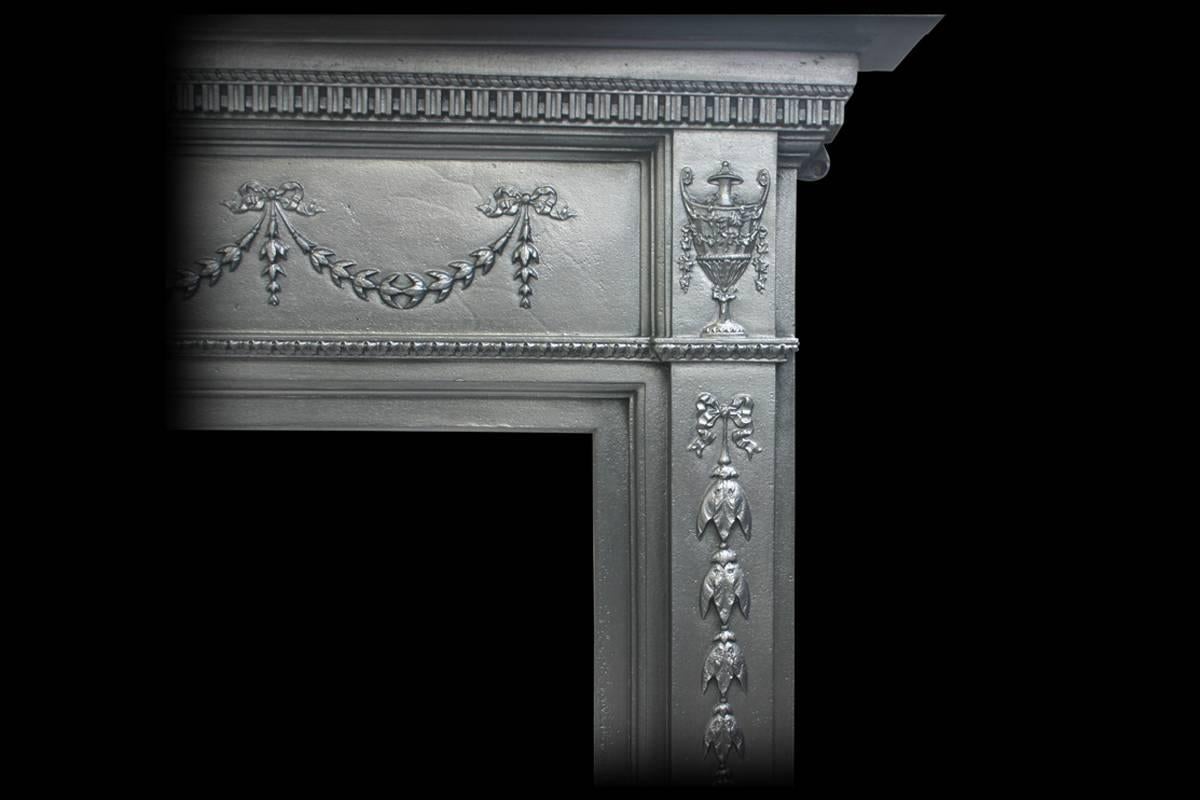 Antique Edwardian neoclassical cast iron fireplace surround with swag decoration to the frieze and urn capitals above bellflower decorated legs, circa 1900.