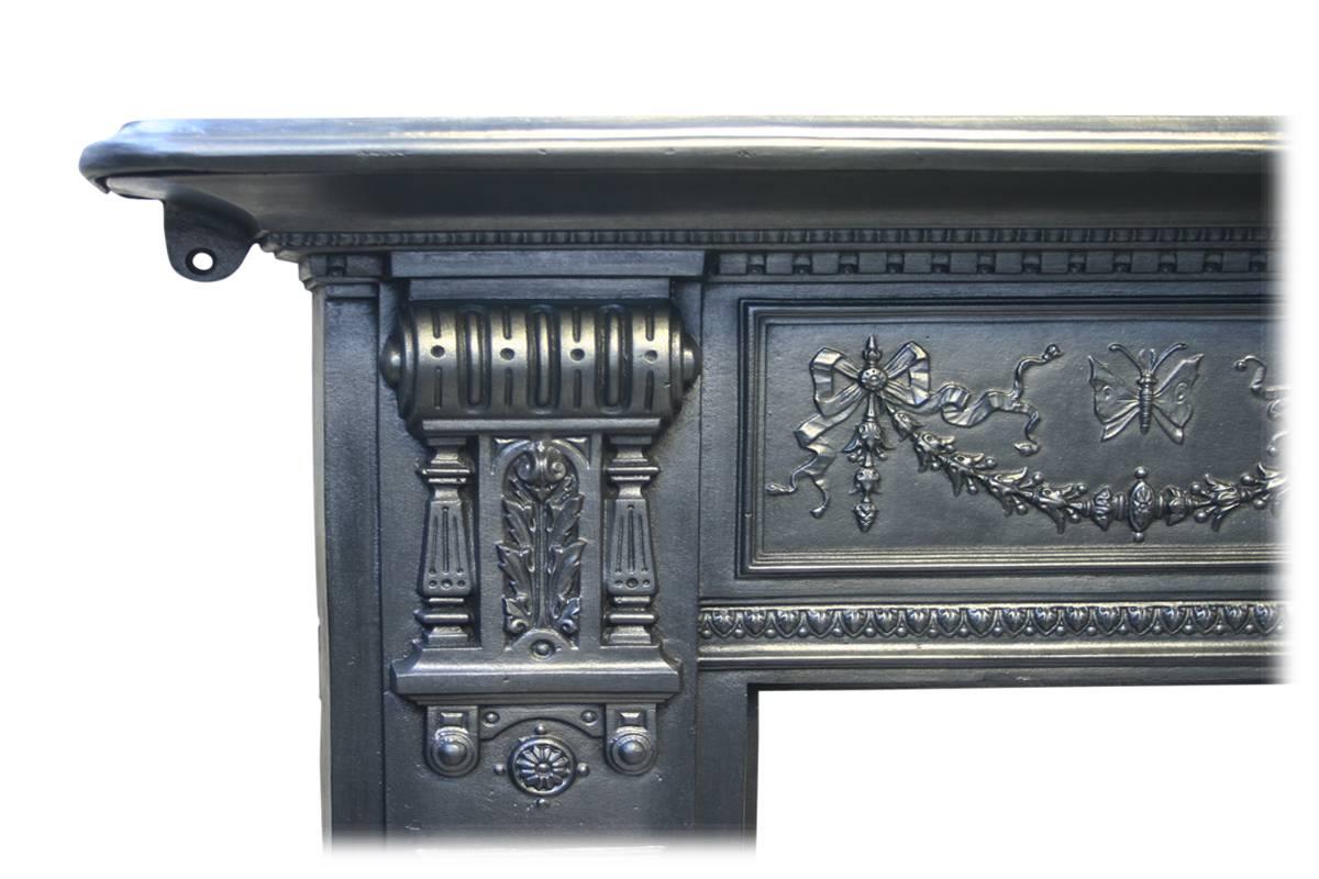 Antique 19th century Arts & Crafts cast iron fireplace surround with ornate corbels supporting the shelf. The frieze in centred by a square plaque cast with a winged girl, flanked by further two panels of bows and swags of bell flowers below a
