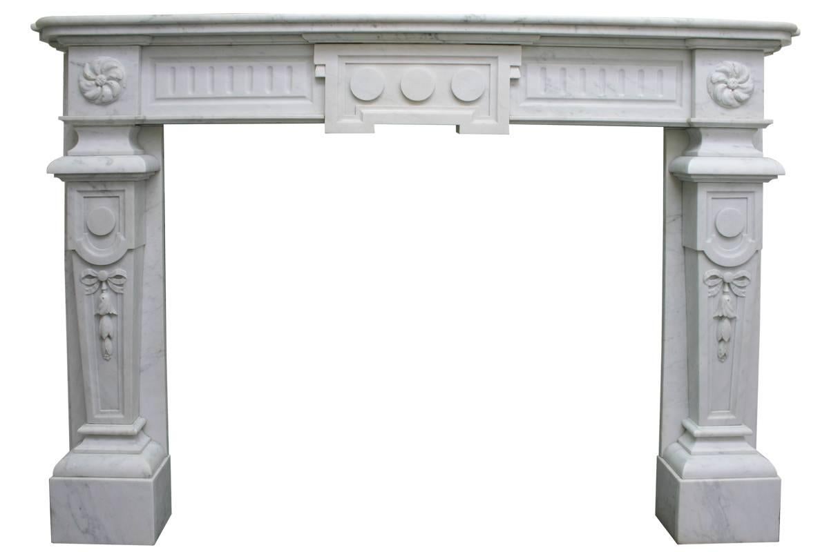 A substantial antique continental white marble fireplace surround. The deep shelf sits above a breakfront frieze. The central tablet displaying three discs is flanked by two reeded panels, terminating in square capitals carved high relief above well