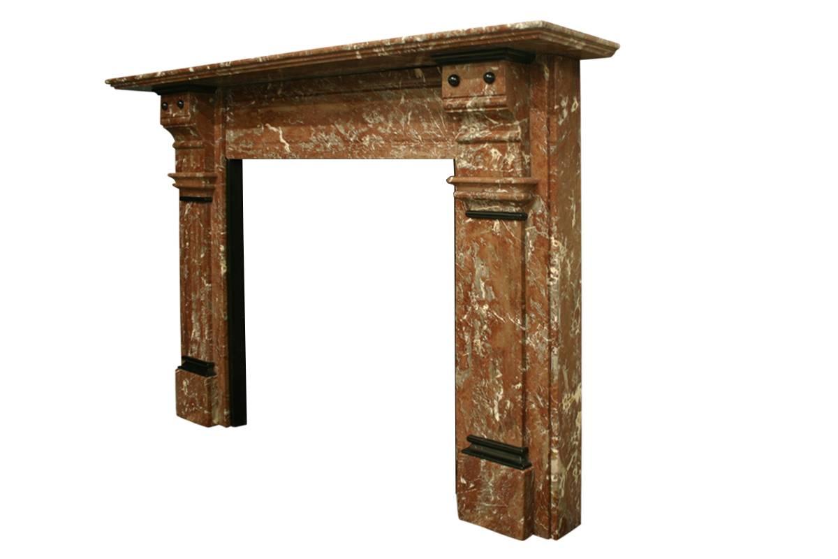 Substantial Victorian Rouge marble fireplace surround the carved corbels having applied black marble bosses above fluted jambs and square plinths also capped with black marble decoration. Fluted panel to the frieze and a double thickness shelf all