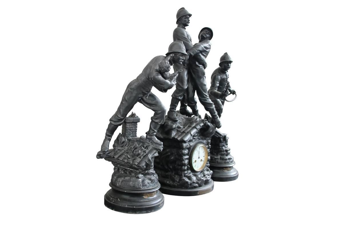 Antique French spelter clock set, circa 1900. The spelter mounted mantel clock is surmounted with a fireman rescuing his colleague, titled 'Victorie Du Devoir' (Victim of Duty), 76cm high approximately. Another titled 'Sauvee' (Saved) depicting a