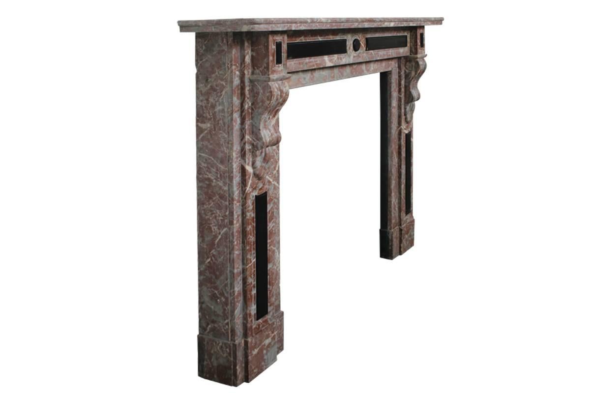 Late 19th century Louis XVI style antique marble fireplace surround in rouge marble. The twin thickness rectangular shelf is set above a panelled frieze with applied Belgium black marble lozenges which is flanked by a pair of square capitals also