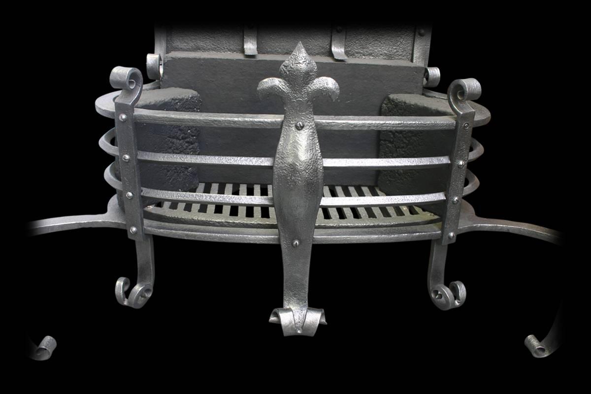 Large antique Arts and Crafts wrought and cast iron fire basket supported by wrought iron standards with splayed feet terminating in well worked flowers flanking the D shaped grate with extra scrolled supports. The cast iron back benefits from