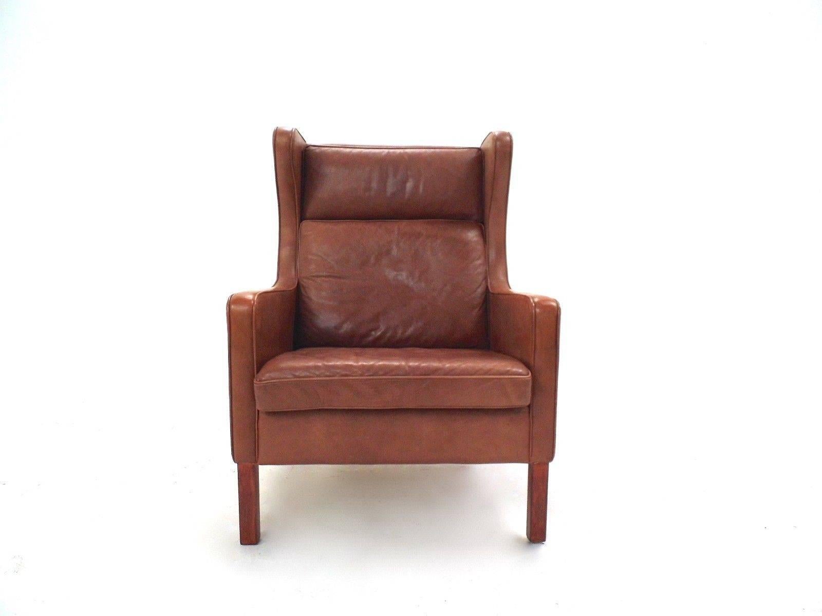 A beautiful chestnut tan brown leather highback armchair by Stouby Polster Mobelfabrik of Denmark, this would make a stylish addition to any living or work area. The chair has a wide seat pad and padded armrests for enhanced comfort. A striking