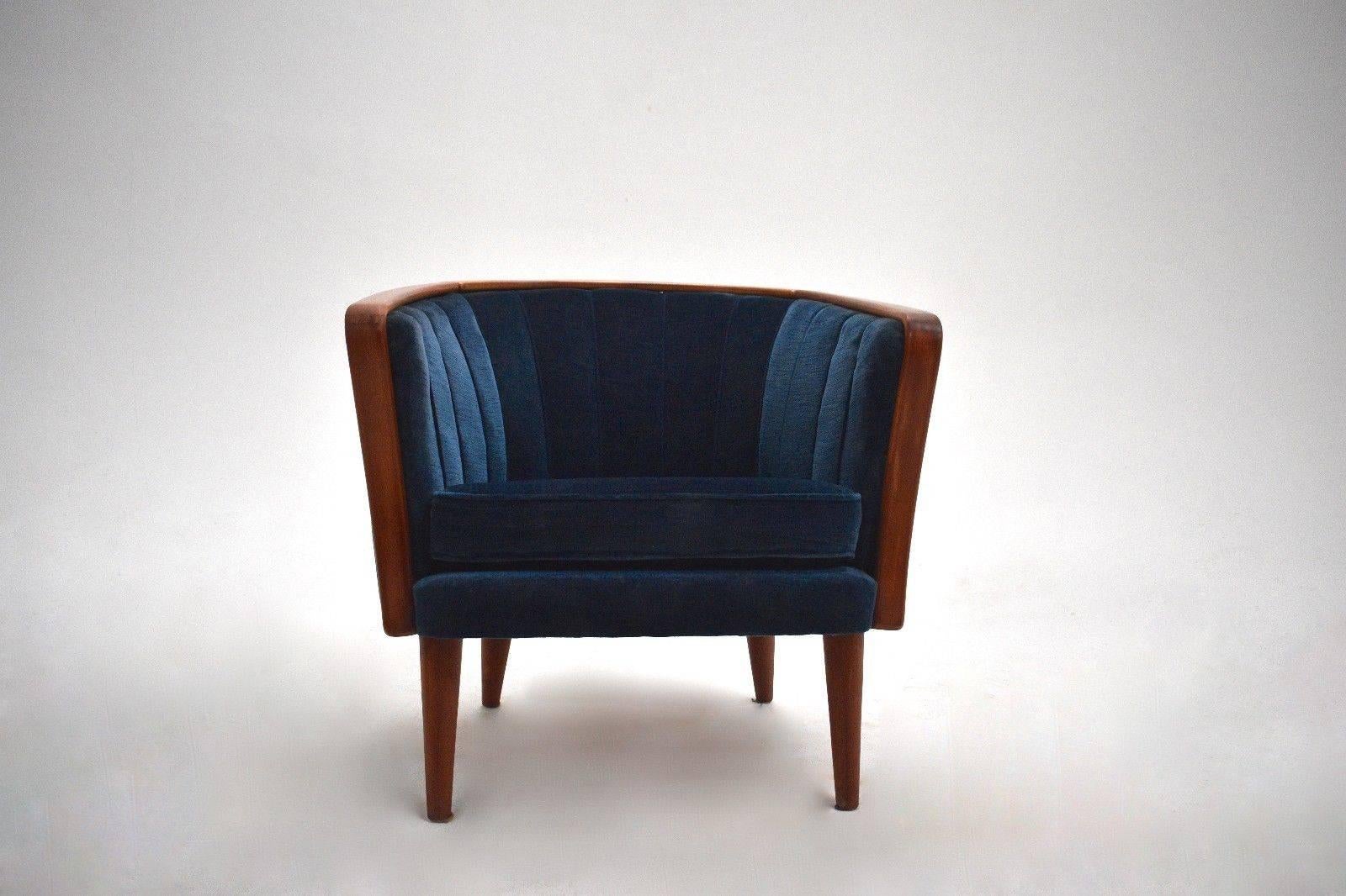 A beautiful Norwegian navy blue velvet club armchair, this would make a stylish addition to any living or work area. The chair has a curved backrest and sculptured wooden armrests for enhanced comfort. A striking piece of Classic Scandinavian