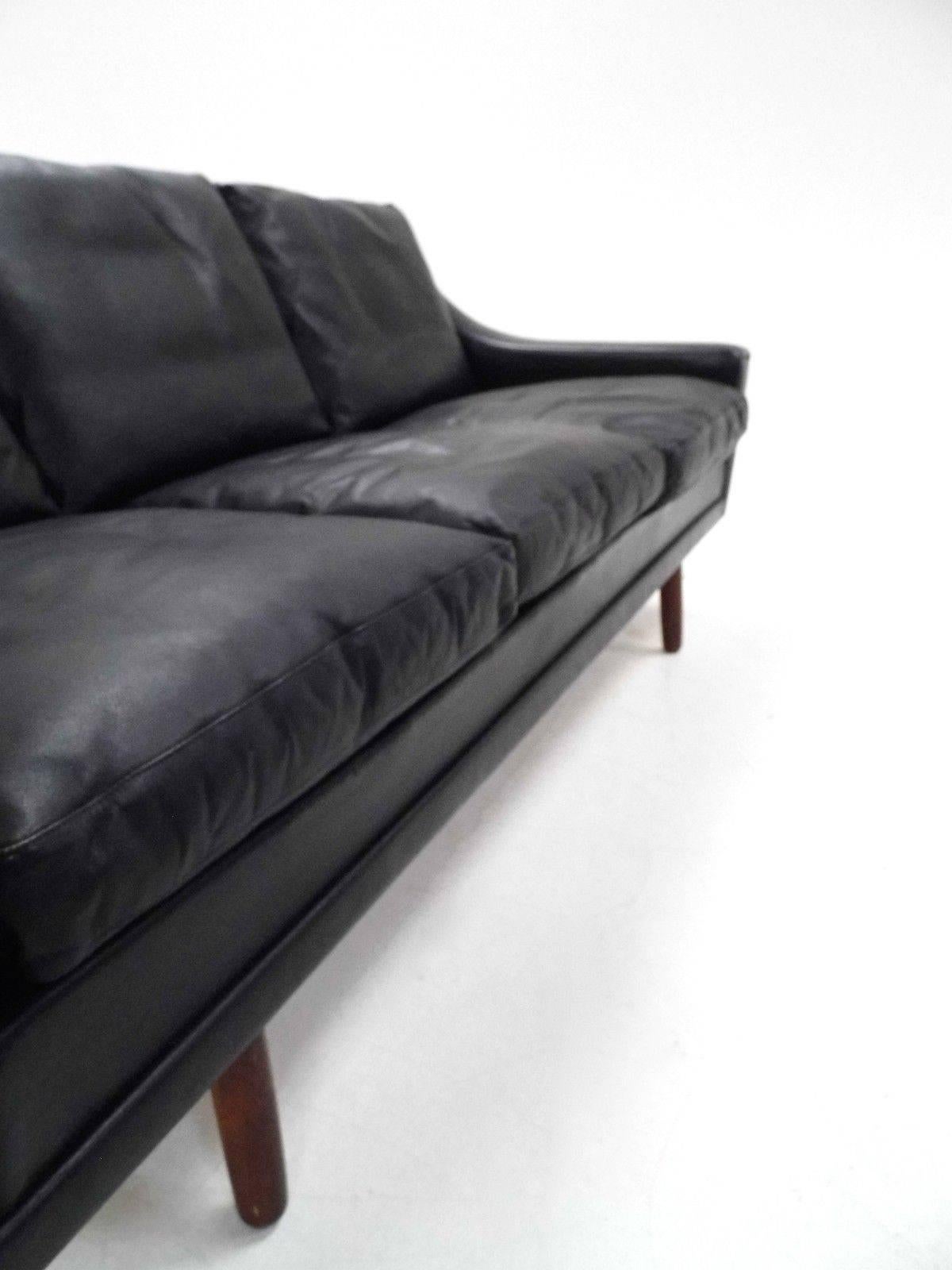 A beautiful Danish black leather and rosewood three-seat sofa, this would make a stylish addition to any living or work area. The sofa has wide cushions and sculptured padded armrests for enhanced comfort. A striking piece of classic Scandinavian
