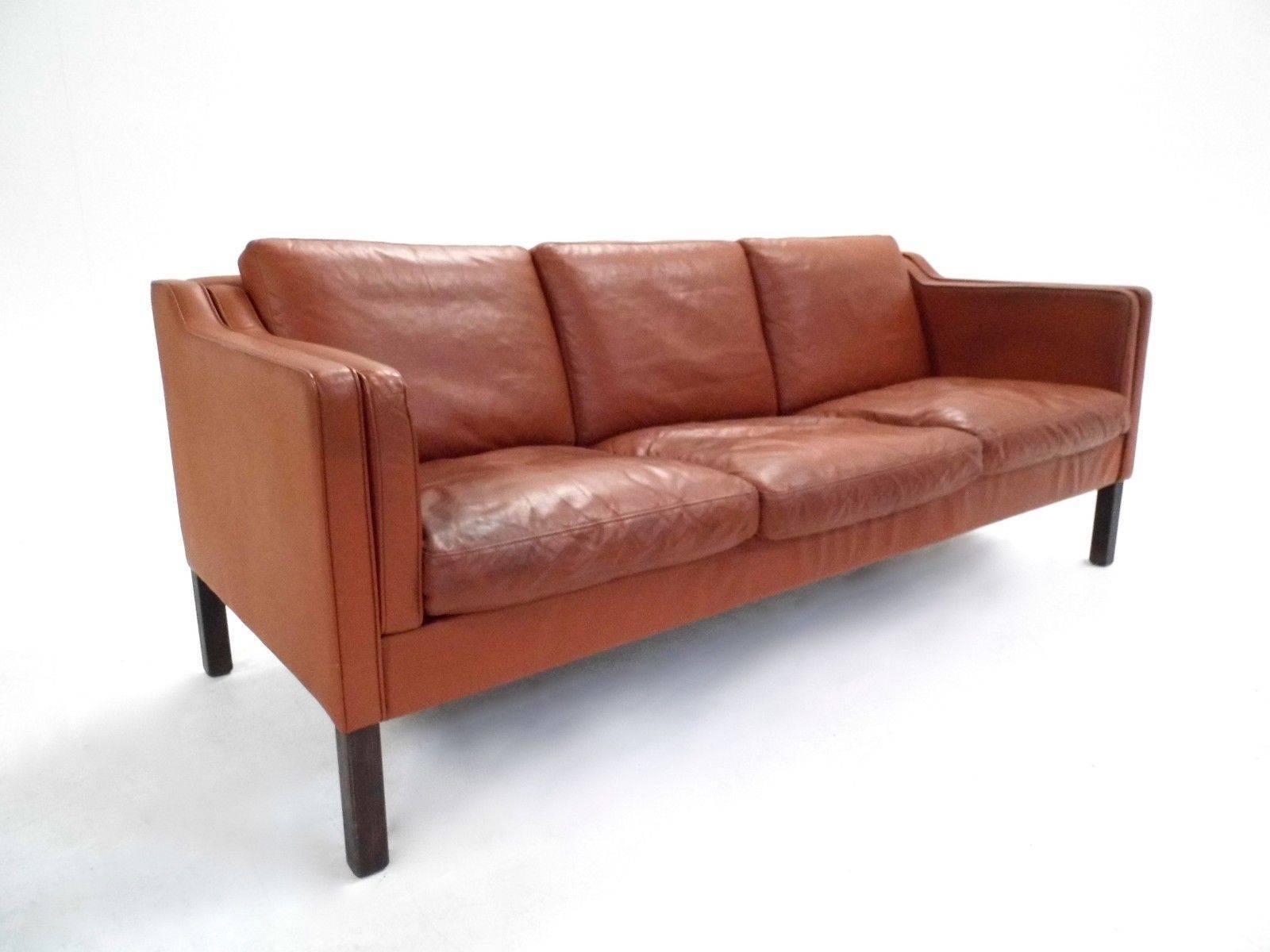 A beautiful Danish tan brown leather three-seat sofa, this would make a stylish addition to any living or work area. The sofa has wide cushions and sculptured padded armrests for enhanced comfort. A striking piece of classic Scandinavian