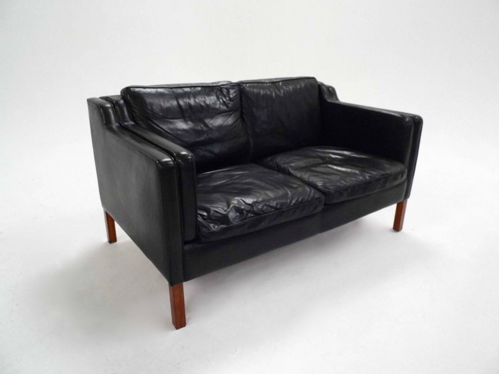 A beautiful Danish black leather two-seat sofa by Stouby, this would make a stylish addition to any living or work area. The sofa has wide cushions and sculptured padded armrests for enhanced comfort. A striking piece of Classic Scandinavian