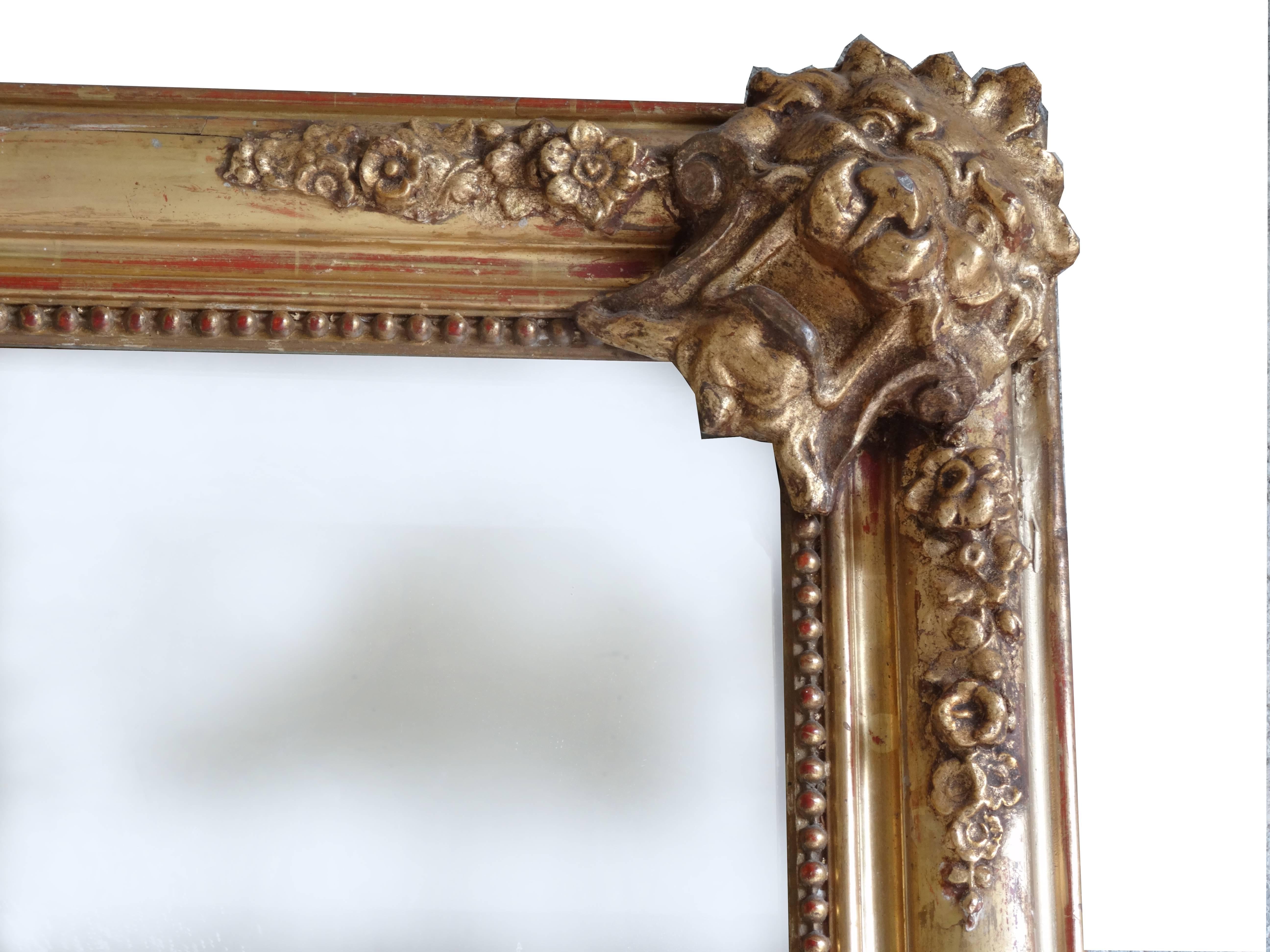 19th century French Regency Style antique mirror; the frame is wood-gilded and the corners are ornate with foliage. A thin row of gilded pearls highlights the framing. The original plate is softly aged. The frame under, shows that the mirror is