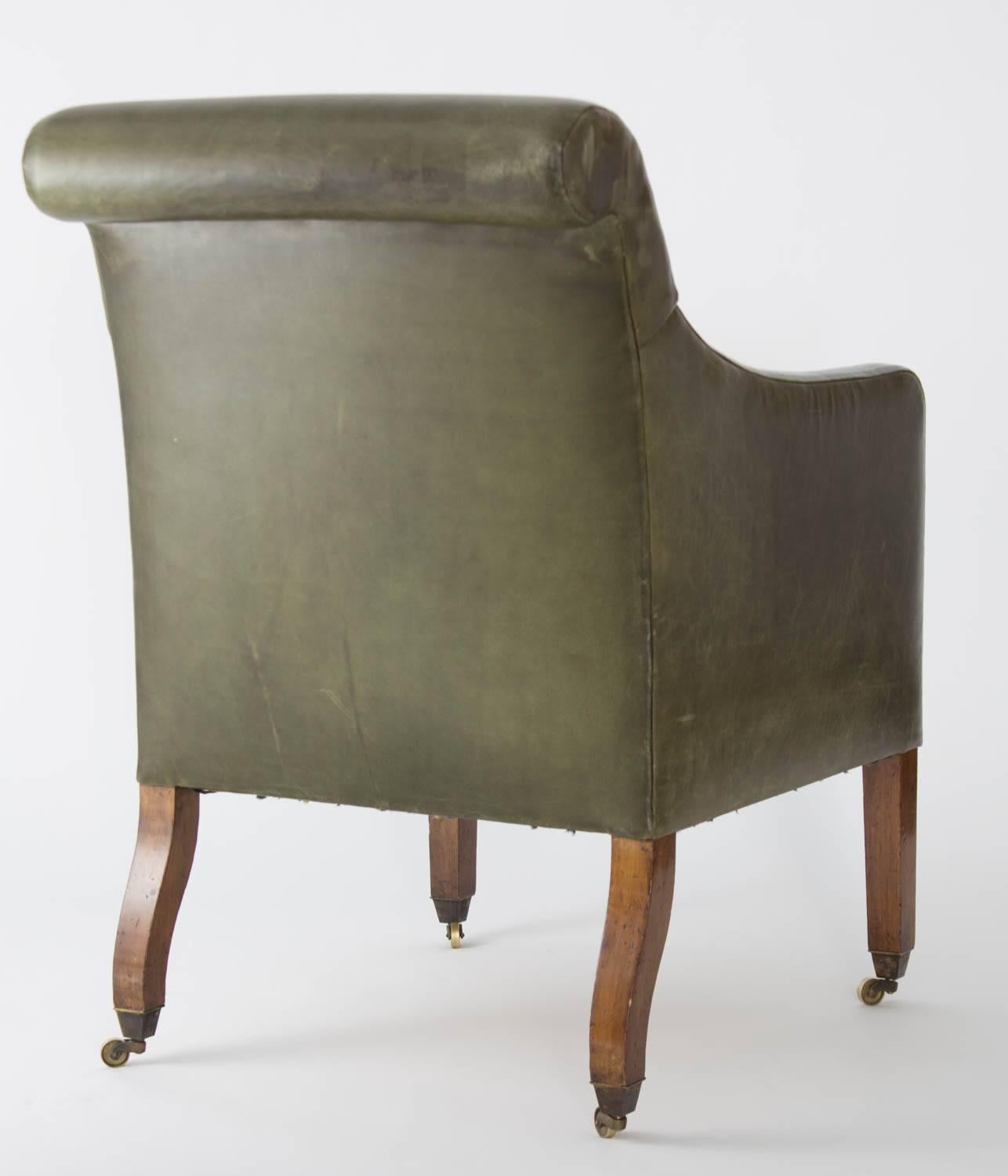 An over scrolled back, arms and loose cushioned seat covered in green leather on fluted Regency legs ending in caps and casters.

Wear consistent with age and use.

Provenance: From the collection of Michael S Smith collection.