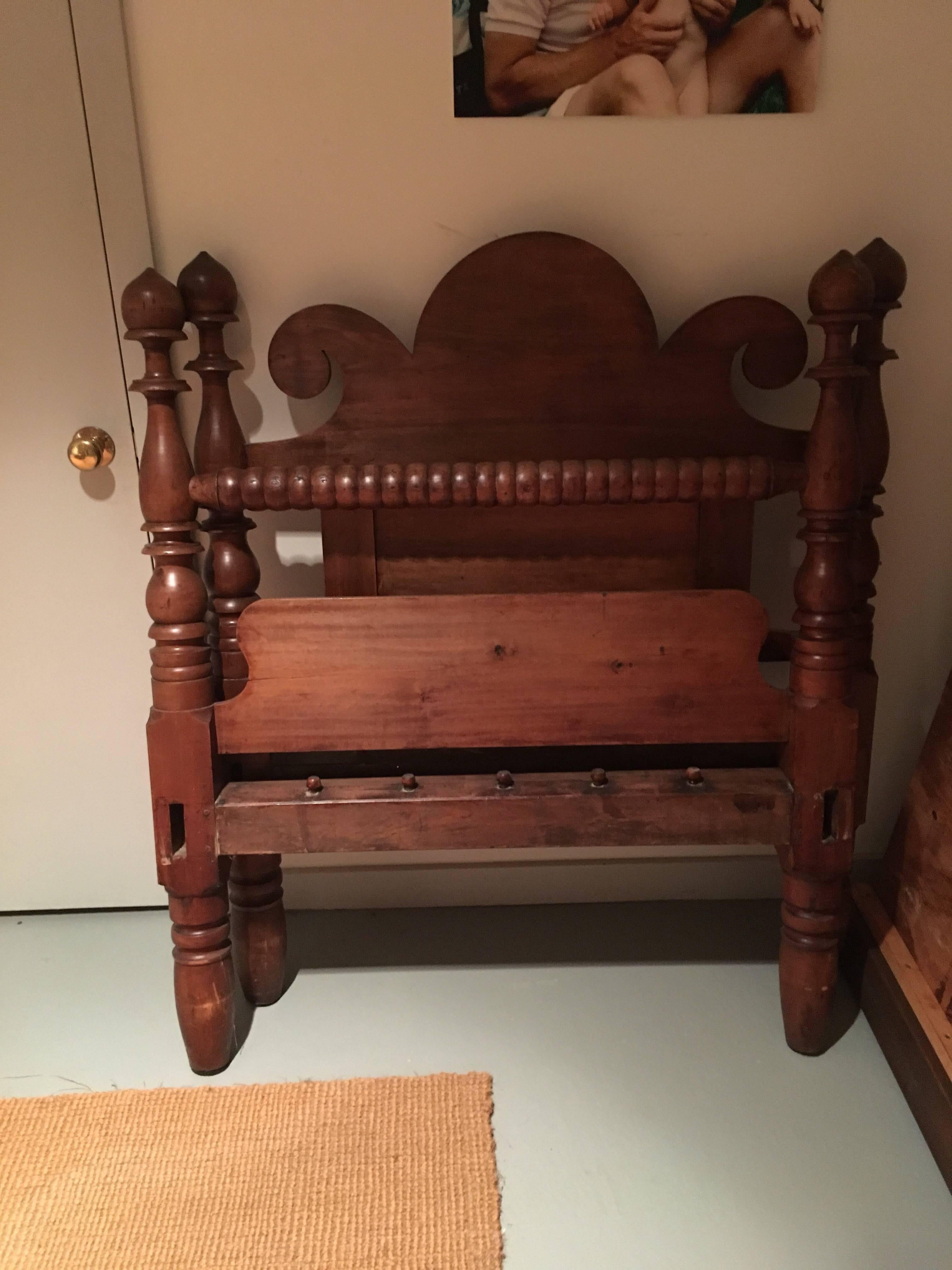 American twin size poster bed with fleur-de-lys-back. This is a very playful design for a twin bed. The headboard is probably from walnut, carved in a fleur-de-lys motif. Footboard has a flat panel on the lower area and a hand-turned bobbin rail at