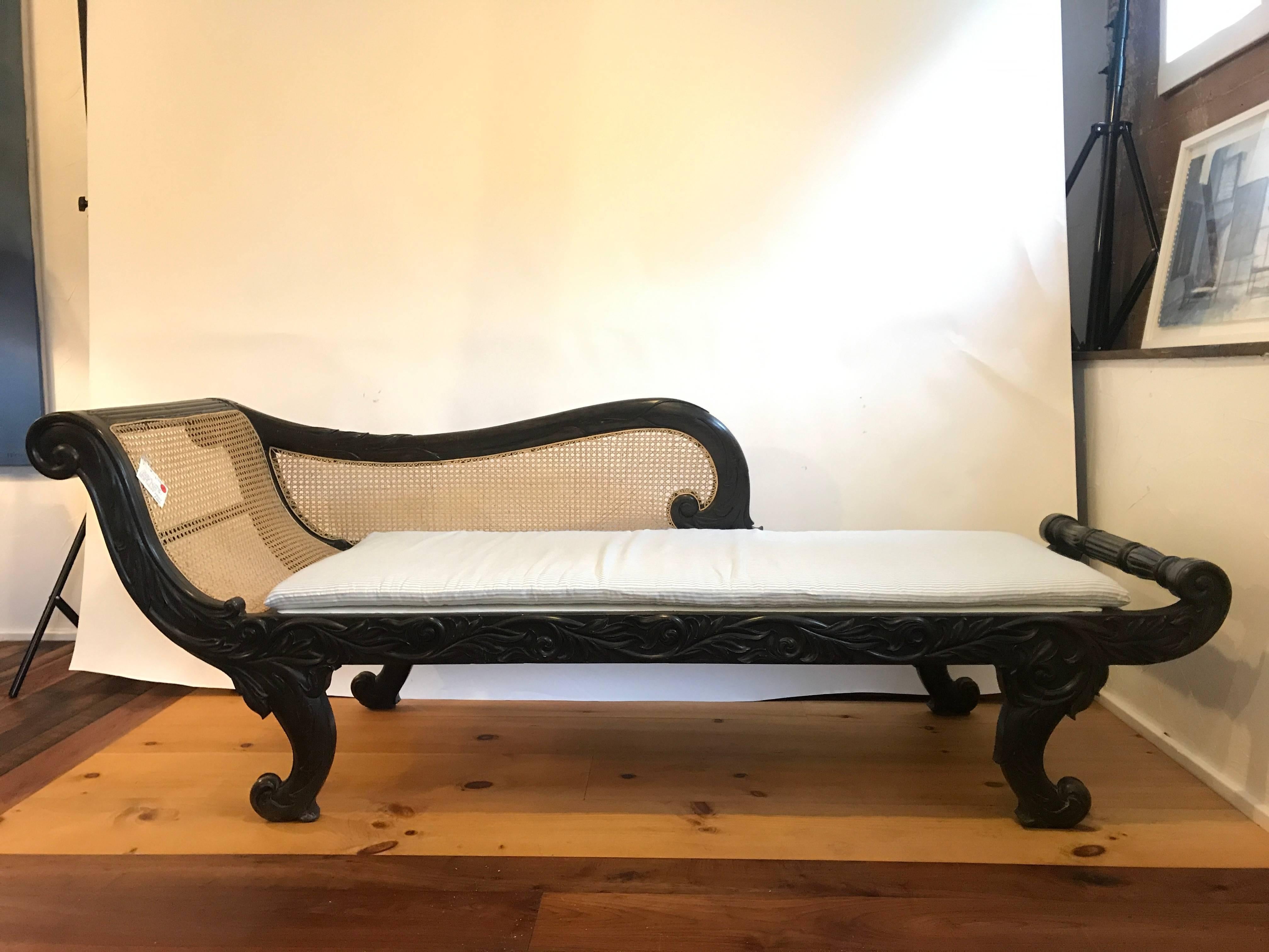 British Colonial chaise lounge from Sri Lanka, circa 1910
Solid carved ebony with caned back and newly upholstered seat in white linen, with a blue and white ticking stripe cushion.

Measures: 28
