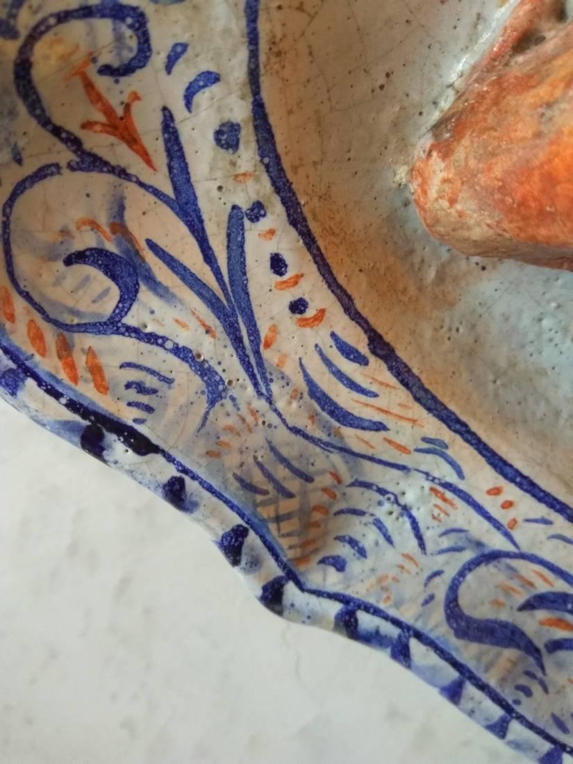 This faience plate with a geometric frieze blue and brown in value the central subject. It is a mullet around which on one arranged an onion and two oysters. The realistic rendering of the colors and the reflections show all the talent of the